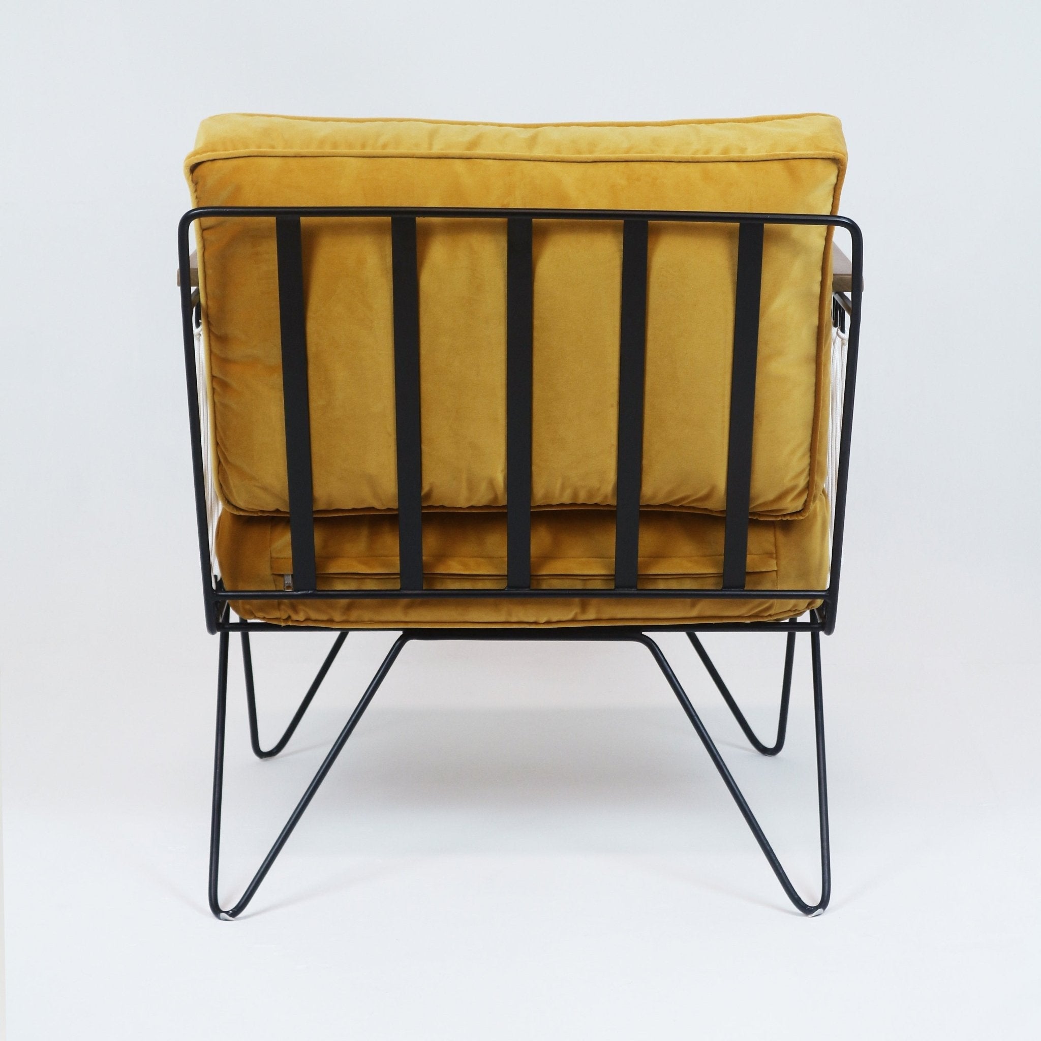 Back view of a modern mustard-yellow fabric lounge chair with plush cushions, black metal slatted frame and hairpin legs.