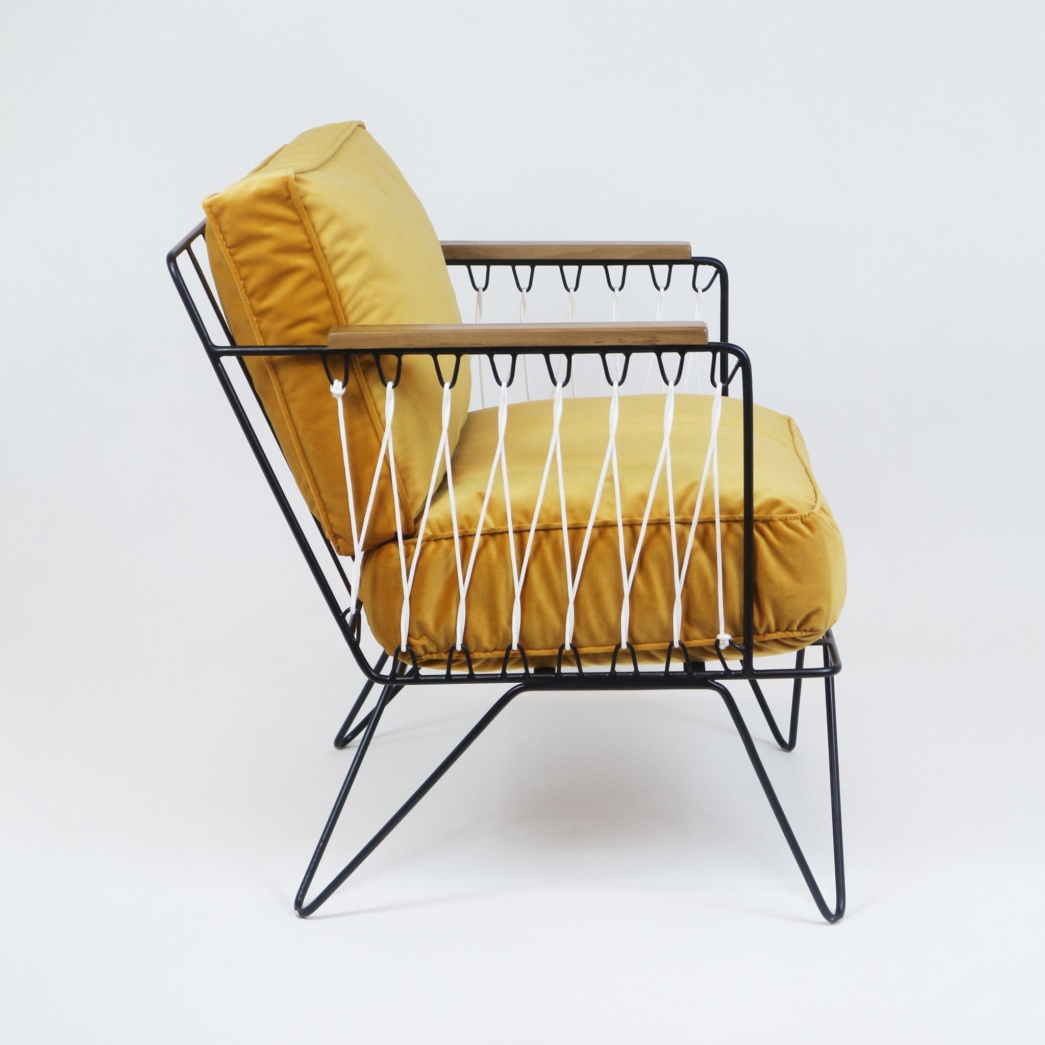 Side view of a modern lounge chair with mustard-yellow fabric cushions, black metal wire frame, white rope lattice sides, and teak arm caps on a plain white background.