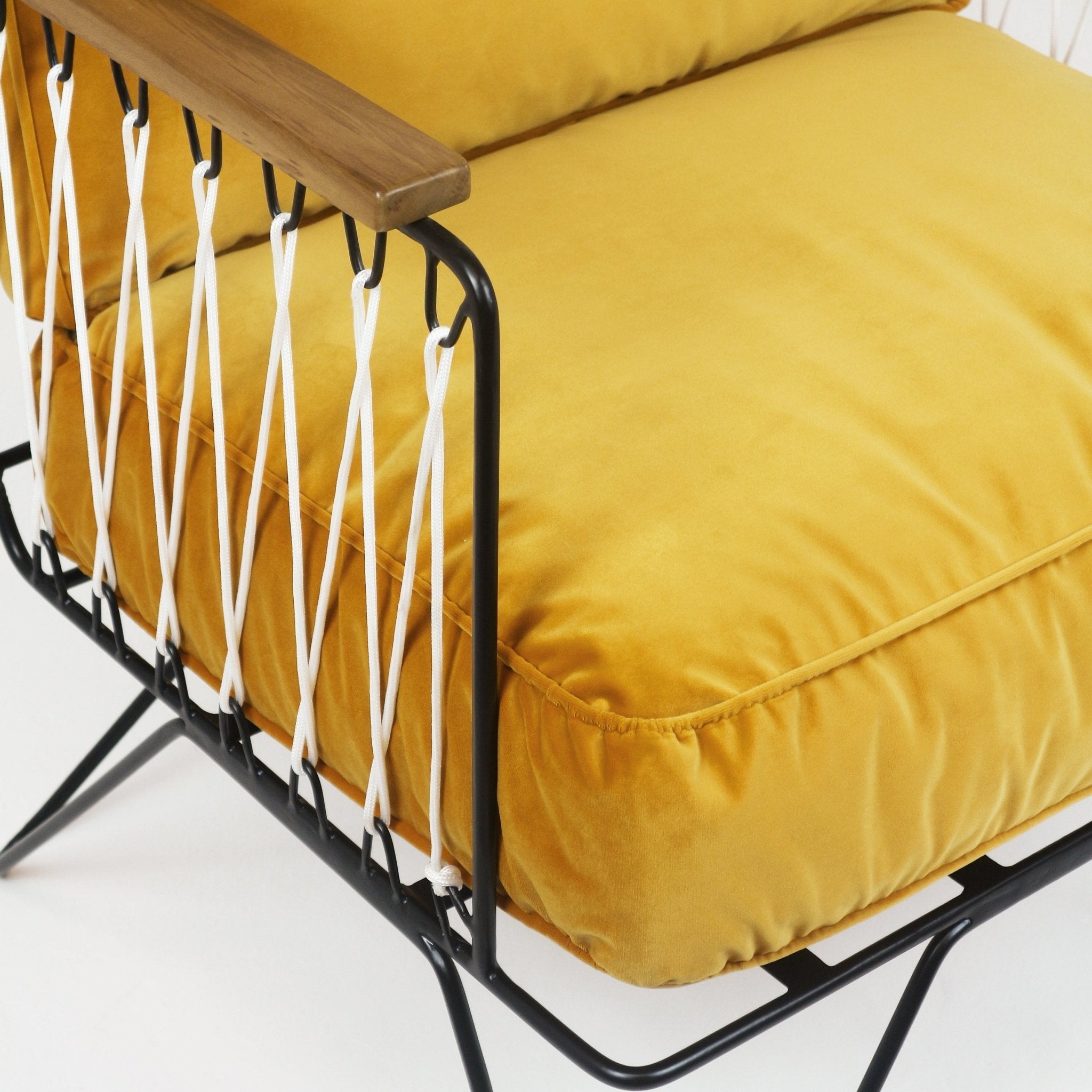 Close-up of a mustard yellow upholstered seat cushion on a black metal chair frame with a teak armrest and white rope woven side detail.