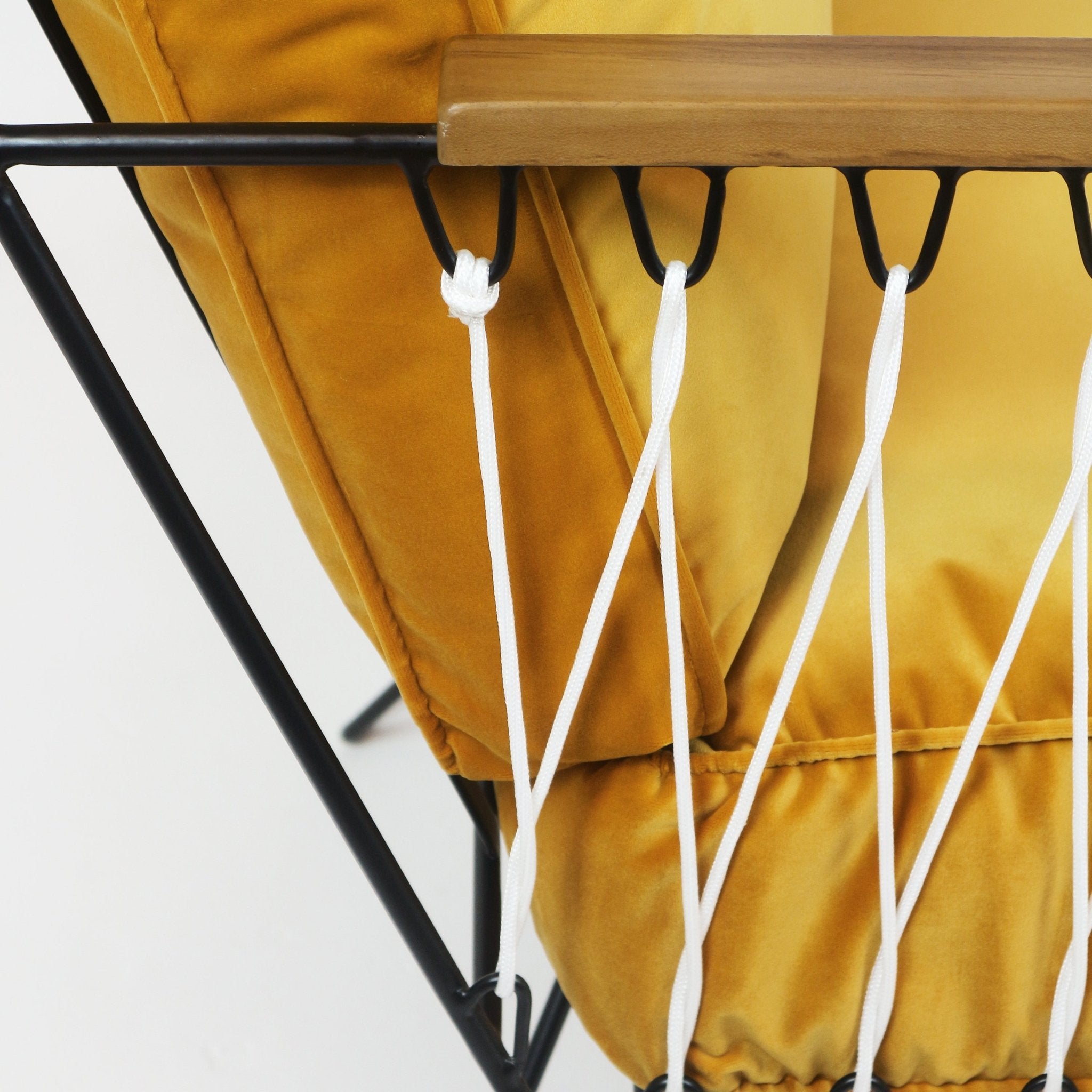 Close-up of a mustard-yellow upholstered fabric cushion tied with white rope lacing to a black metal frame beneath a teak armrest.