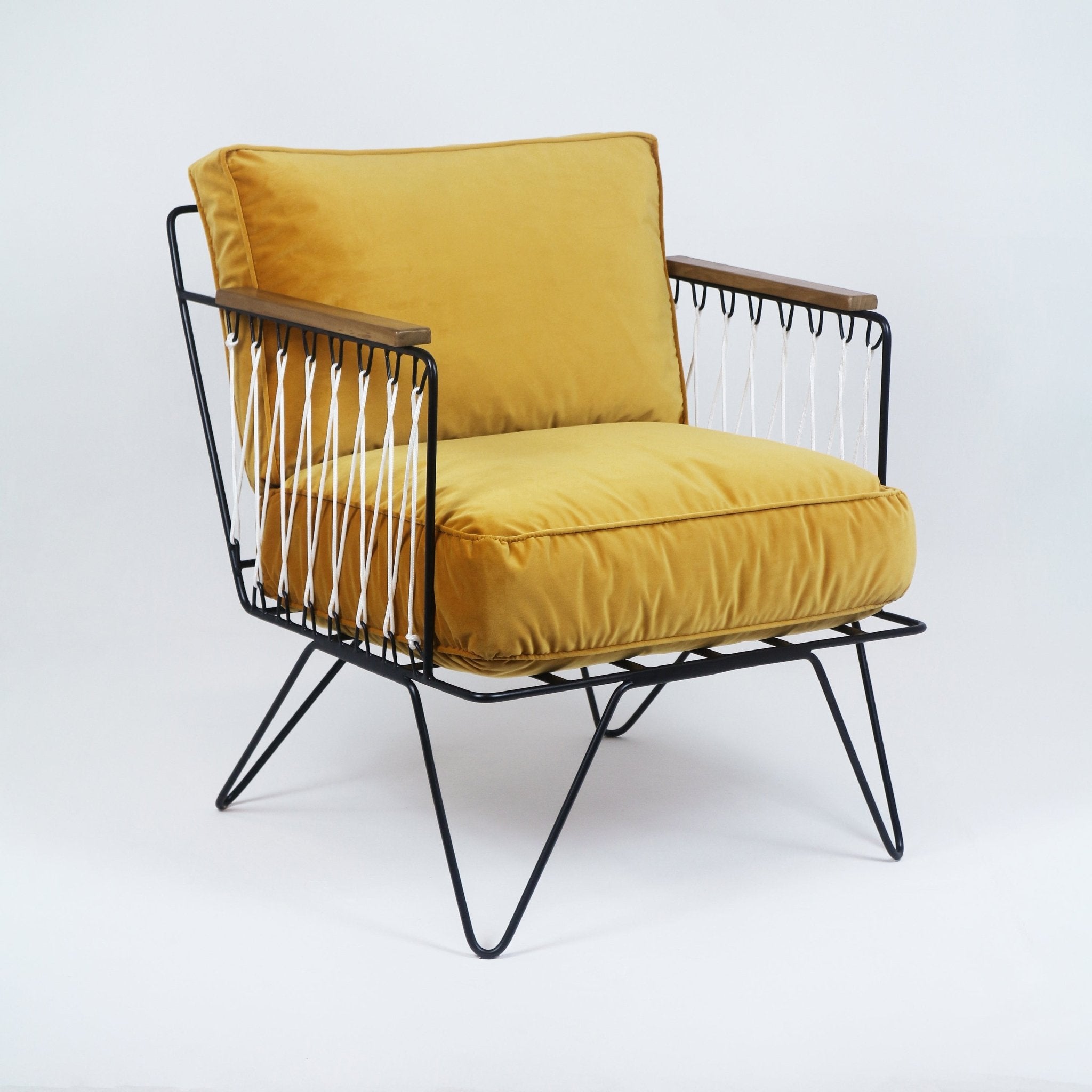 Modern lounge armchair with mustard yellow upholstered seat and back, black metal wire frame and hairpin legs, teak arm caps and white rope detailing along the sides.