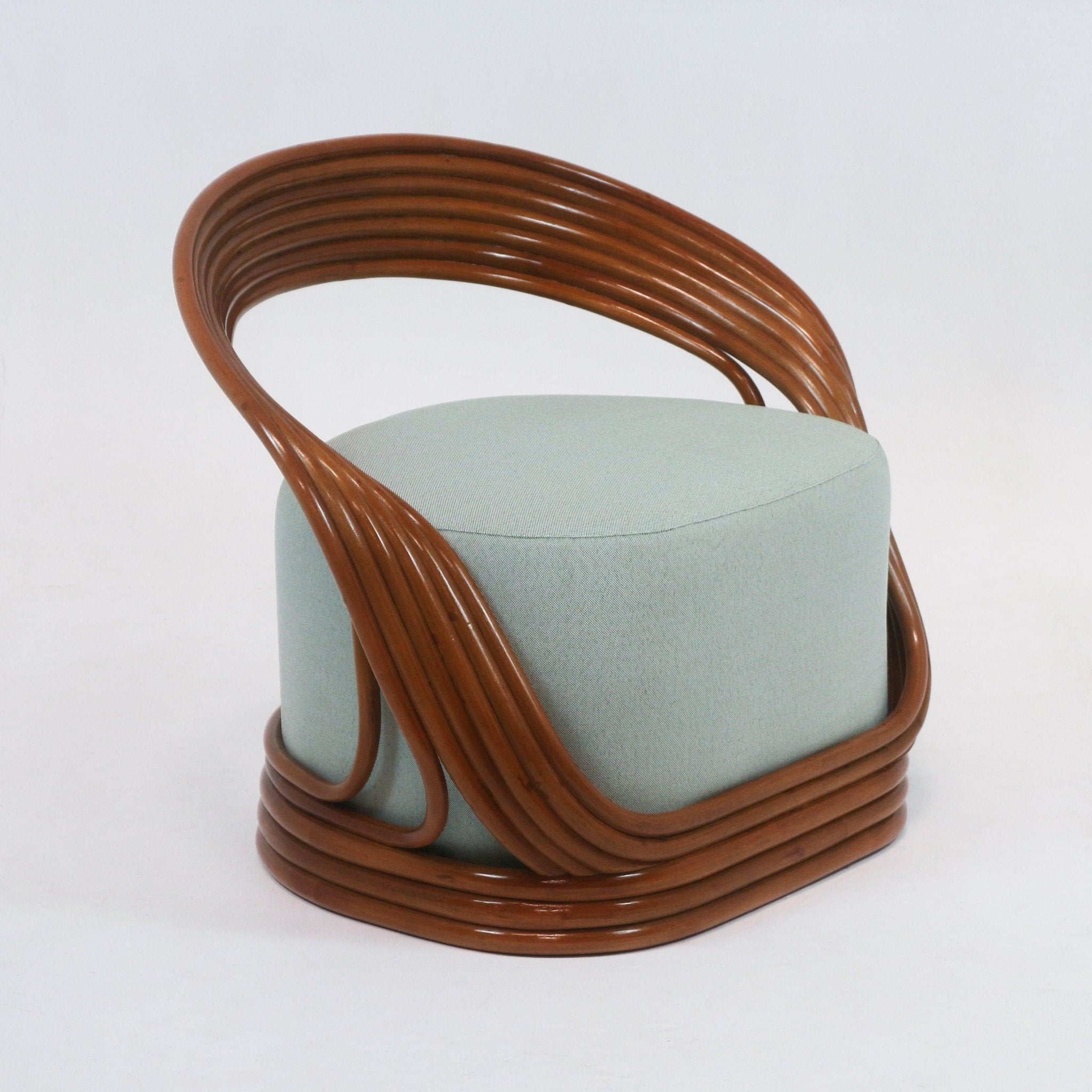 Mid-century modern lounge chair with a glossy brown cane frame that curves around a pale green fabric-upholstered cylindrical seat, featuring layered rattan arms and a wrapped rattan base.