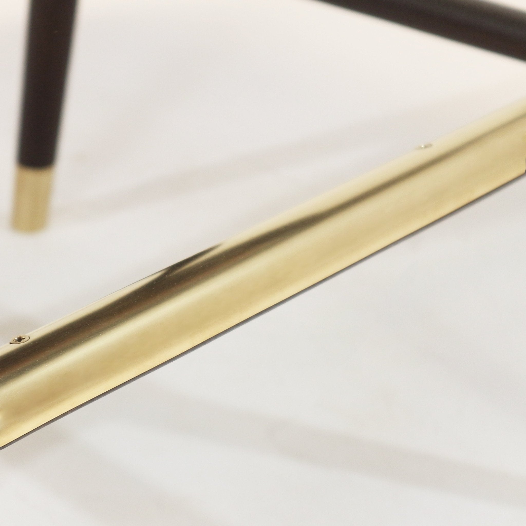 Close-up of a polished brass footrest/stretcher and a dark teak leg with a brass ferrule from a blue upholstered bar stool, shown against a neutral background.