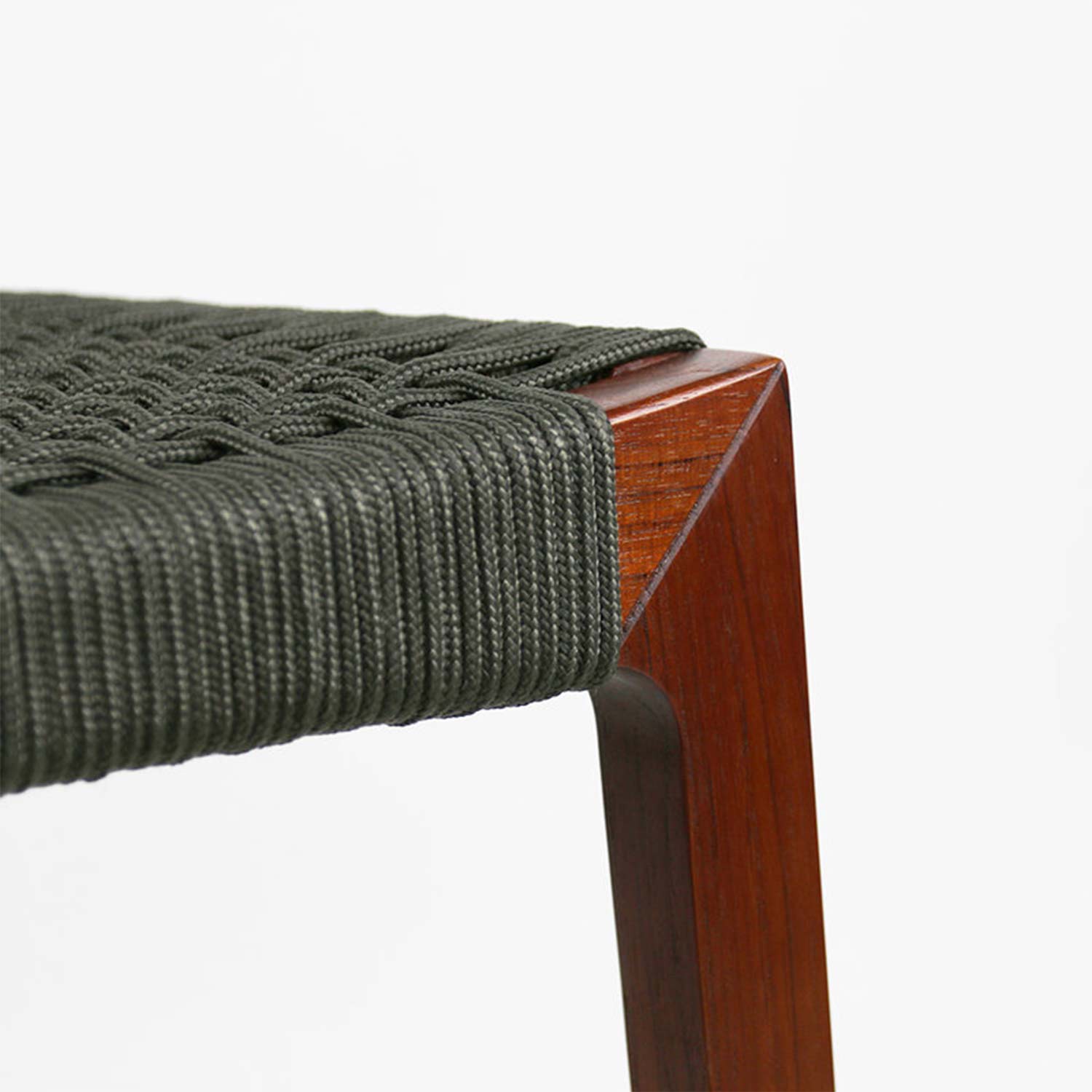 Close-up of a teak bar stool corner showing an olive-gray woven rope seat tightly wrapped over the teak wood frame with a mitered leg detail.