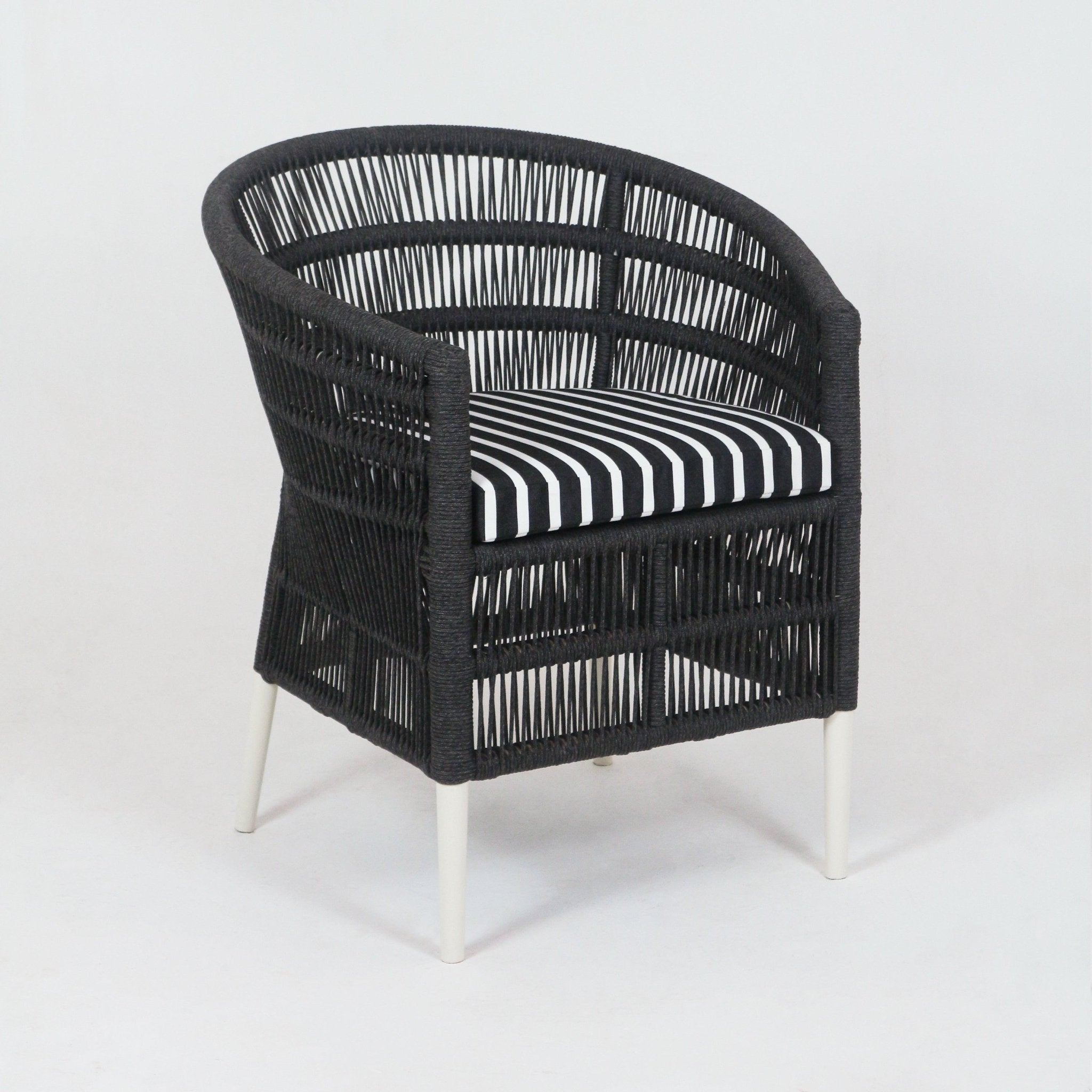 Coastal black woven rope outdoor armchair with white metal legs and a removable black-and-white striped Sunbrella seat cushion, featuring a rounded open-weave back and wrapped arm frames.