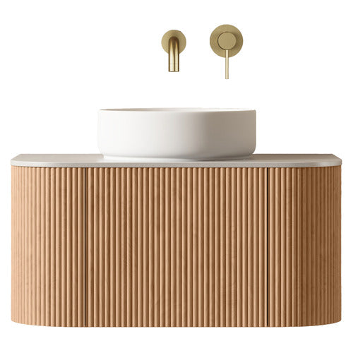 Floating fluted teak wood bathroom vanity with a light stone top and round white ceramic vessel sink, paired with a wall-mounted brushed brass spout and round single-lever control.