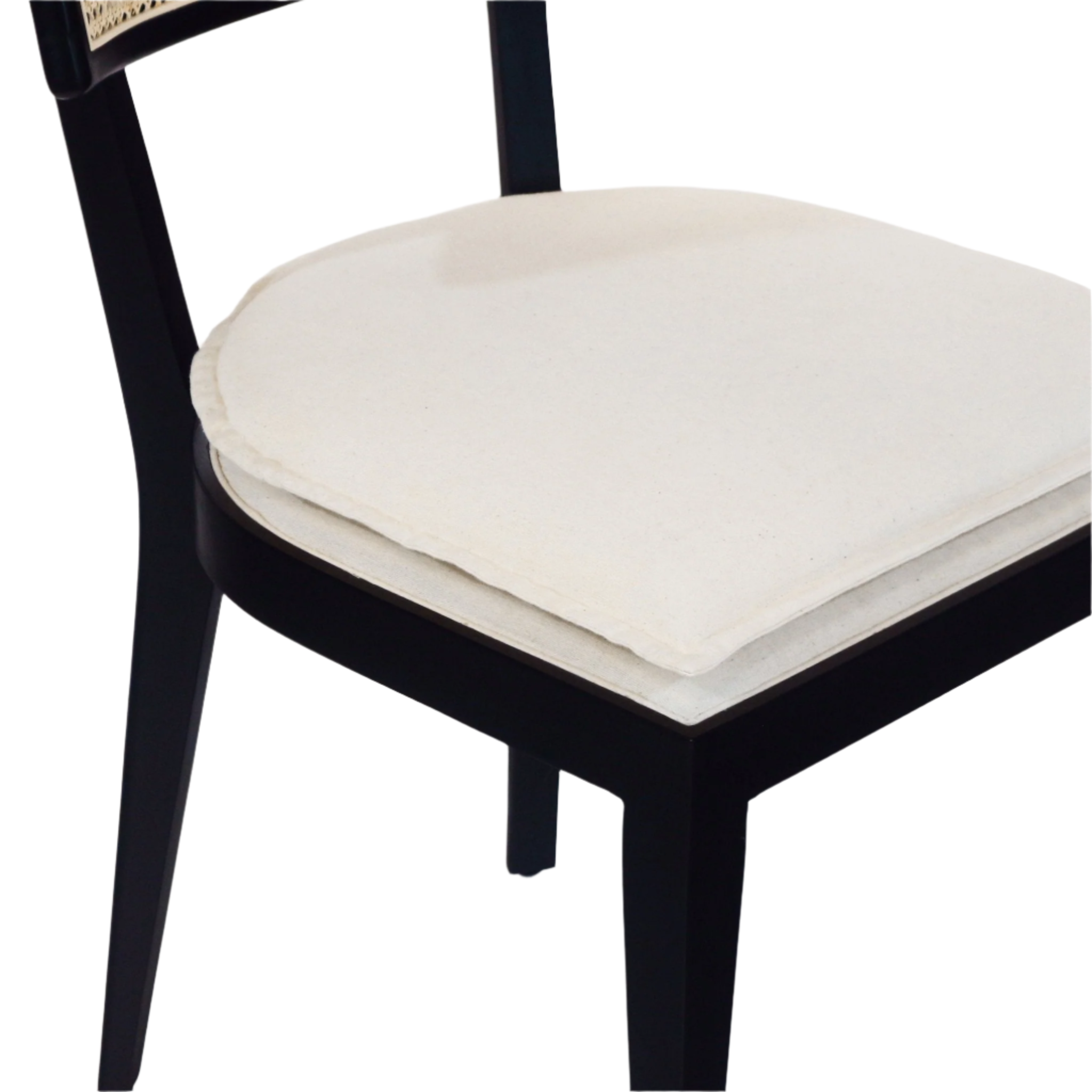 Close-up of a black solid wood dining chair showing a cream fabric upholstered seat with a layered removable seat pad and black tapered legs; a portion of the woven rattan backrest is visible.