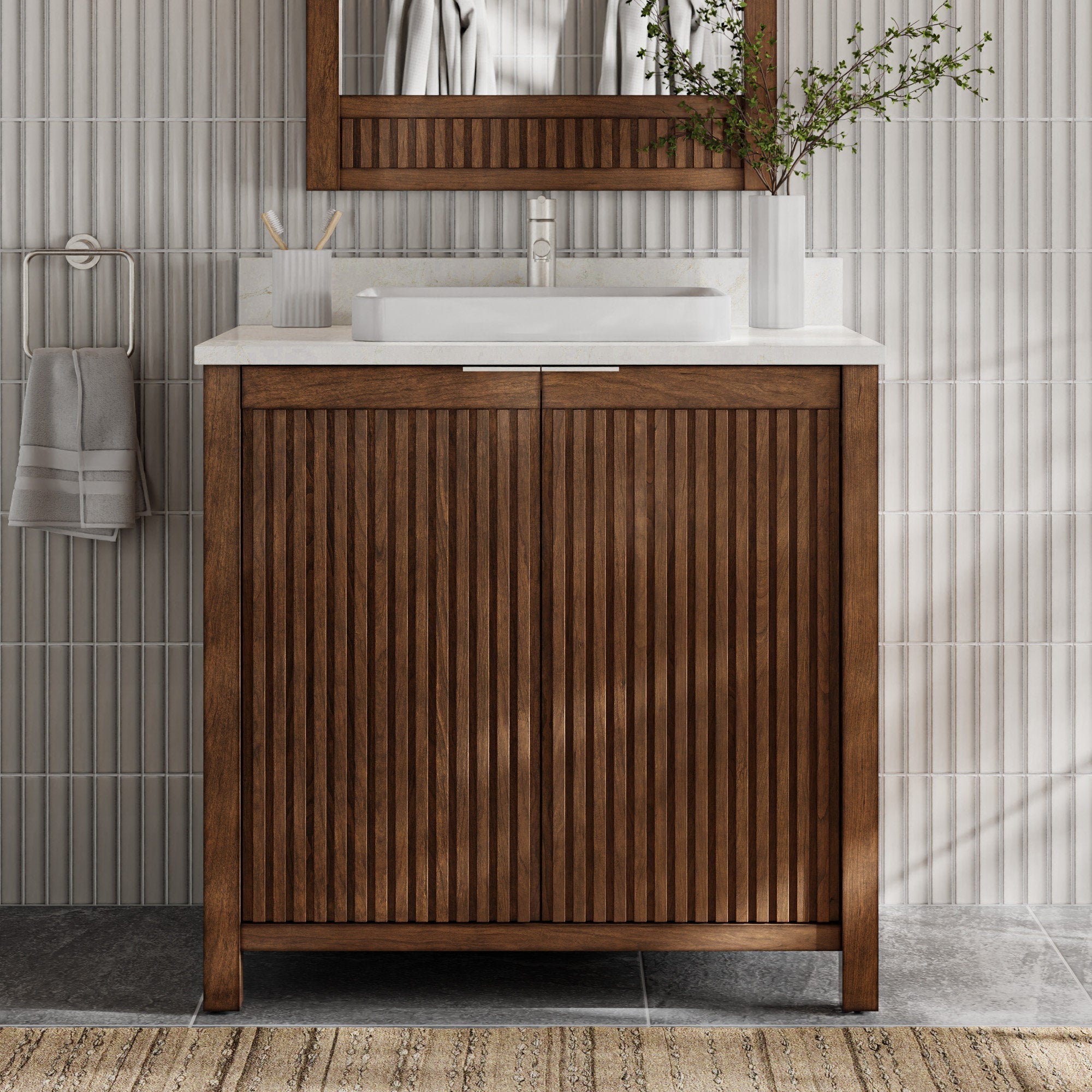 Freestanding modern solid wood bathroom vanity with vertical fluted doors, stone countertop and rectangular white vessel sink with center faucet; wood-framed mirror above, towel on ring and vase with branches.