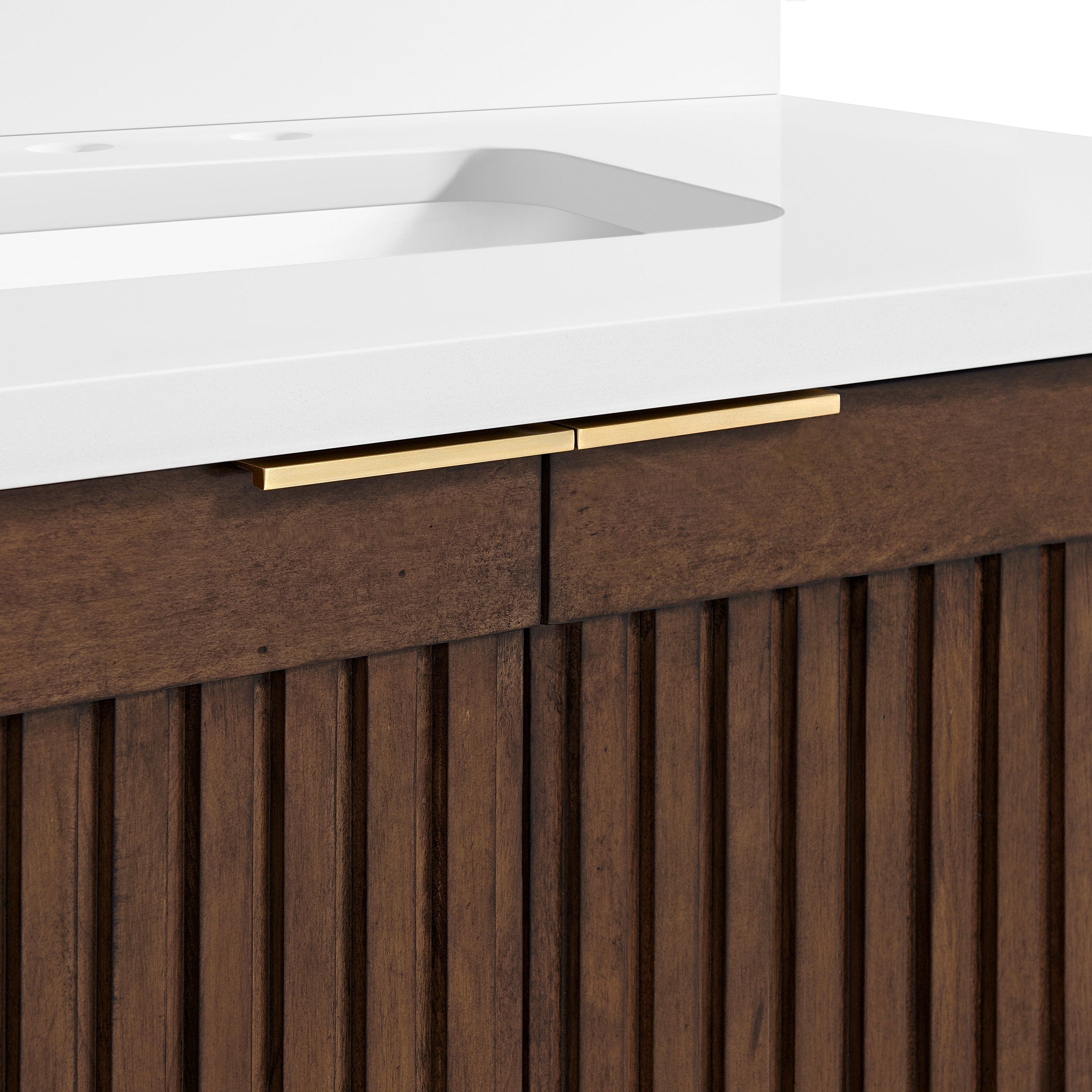 Close-up of a bathroom vanity showing a white stone countertop with integrated rectangular sink, fluted solid wood brown cabinet front and slim gold drawer handles.