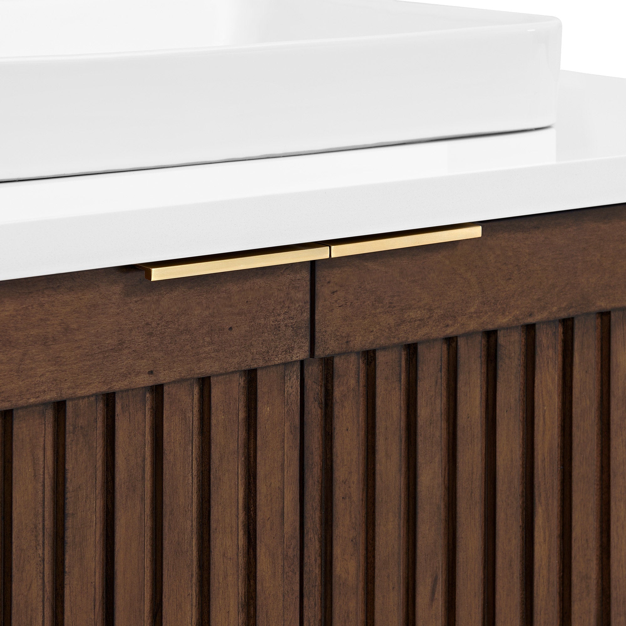 Close-up of a white stone countertop and ceramic sink resting on a natural solid wood fluted bathroom vanity in warm brown, featuring slim brass bar drawer handles.