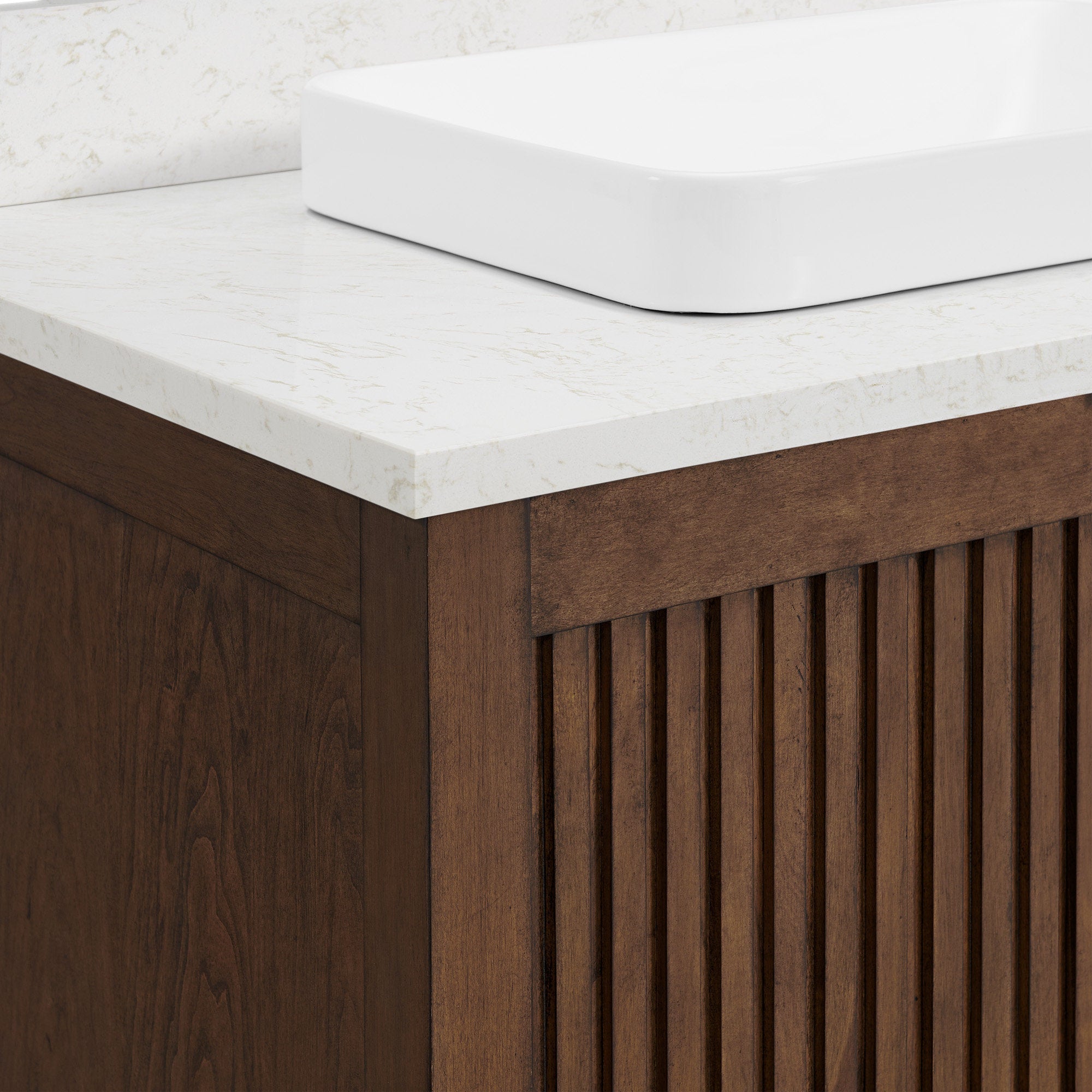 Close-up of a modern solid wood bathroom vanity corner with vertical fluted cabinet detailing, a stone countertop and a white rectangular ceramic vessel sink.