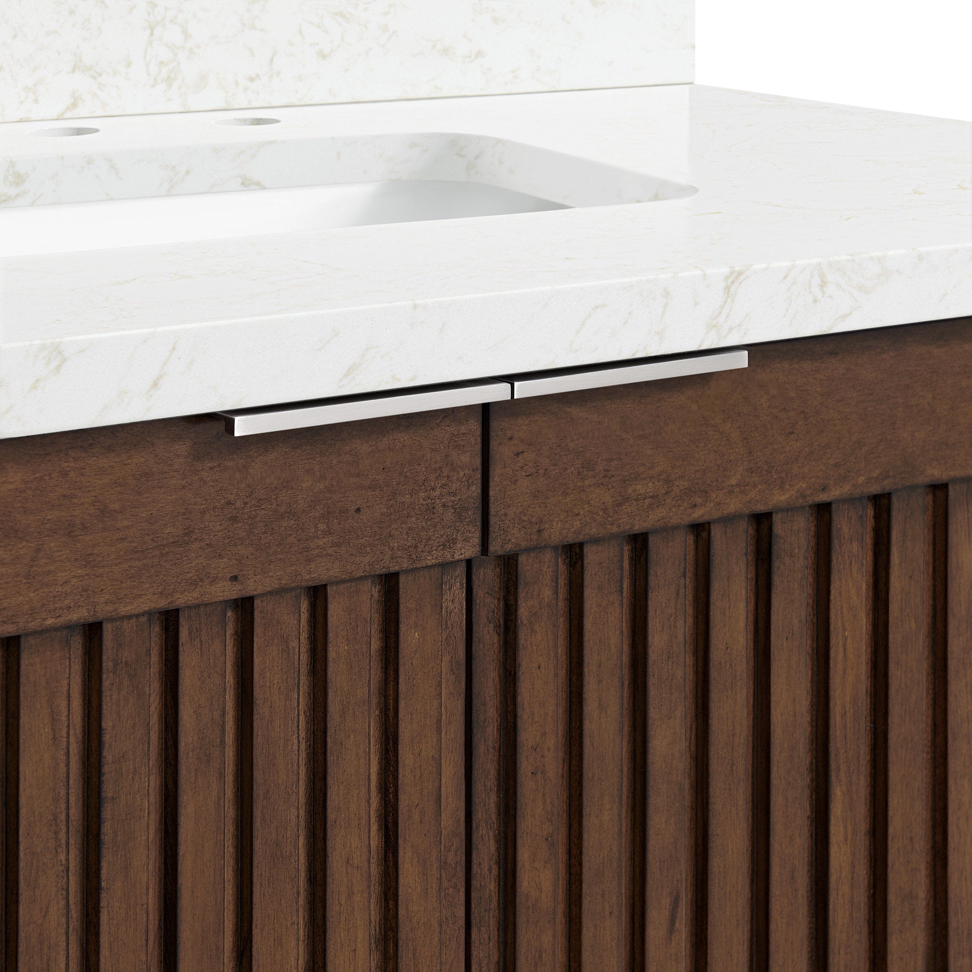 Close-up of a modern stone countertop with subtle marble veining and integrated white basin above a brown natural solid-wood fluted vanity, featuring slim brushed metal drawer handles and faucet cutouts.