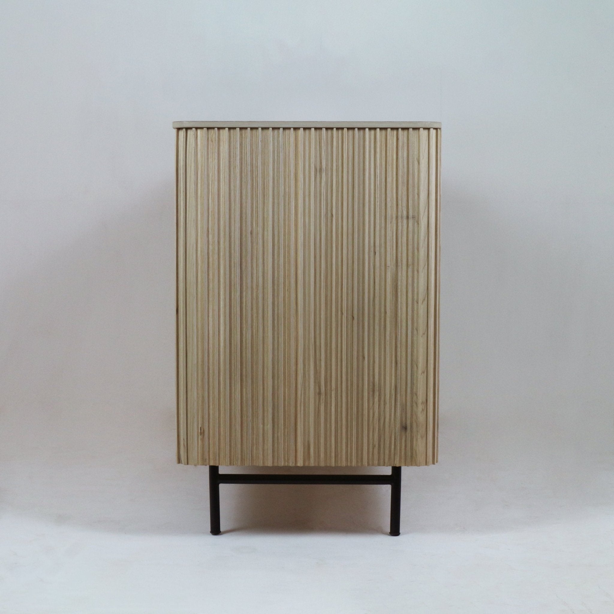 Front view of a tall teak sideboard with vertical fluted slats in a natural finish, raised on a slim black metal base and legs, photographed against a neutral white background.