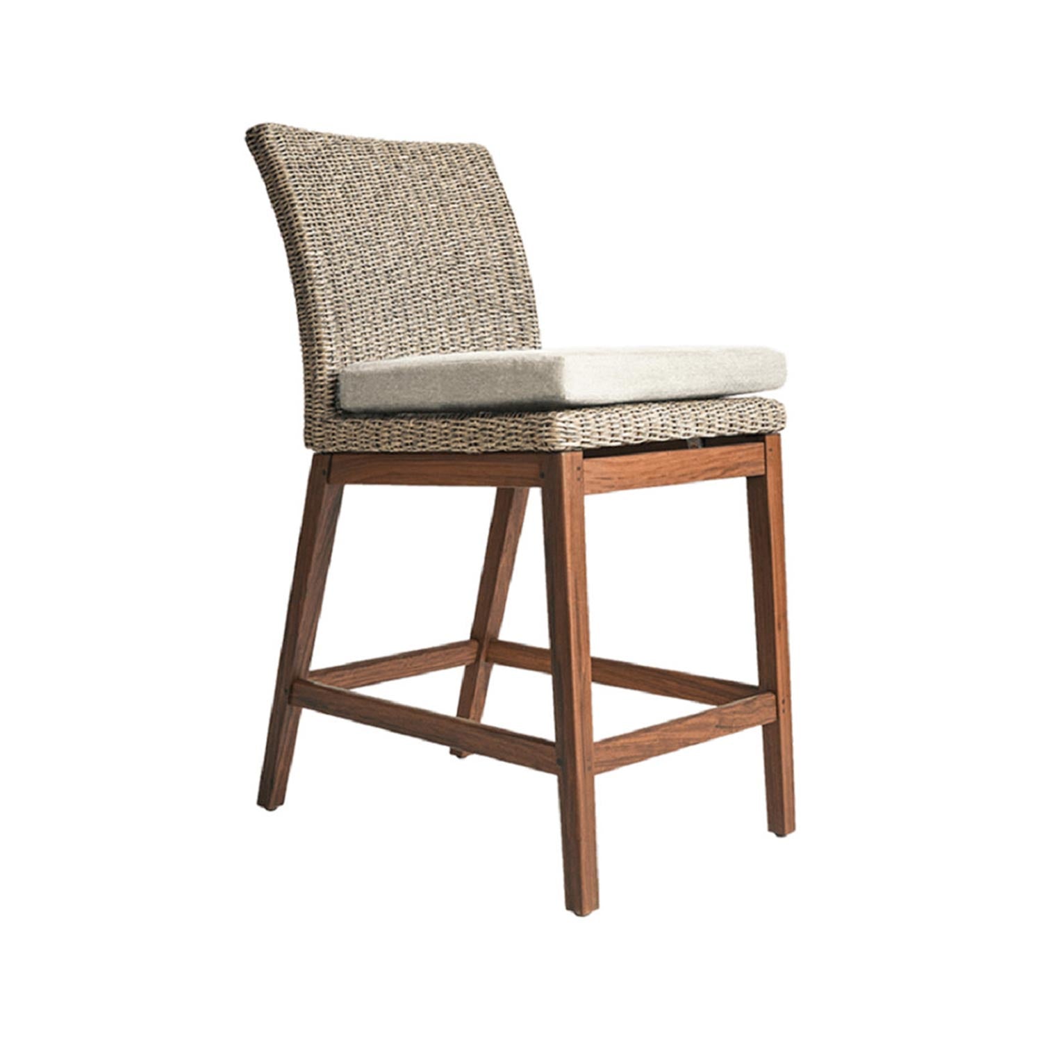 Armless outdoor bar stool with a natural teak frame, woven seat and back, and a beige fabric cushion; angled legs connected by a square stretcher that serves as a footrest.