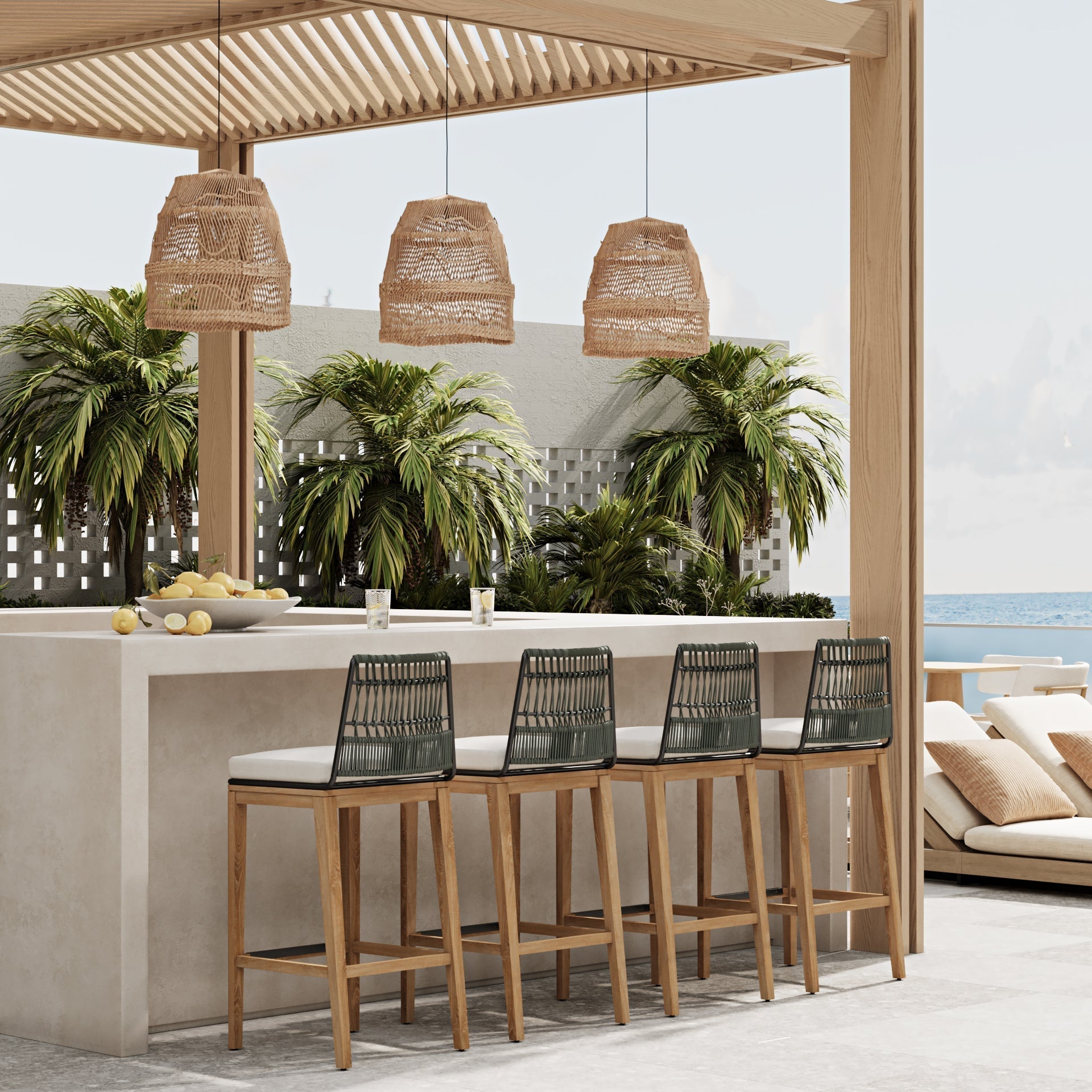 Four mid-century modern outdoor bar stools with teak legs, black woven rope backs and light fabric cushions lined at a concrete bar under a wooden pergola with wicker pendant lights and tropical plants, ocean visible beyond.