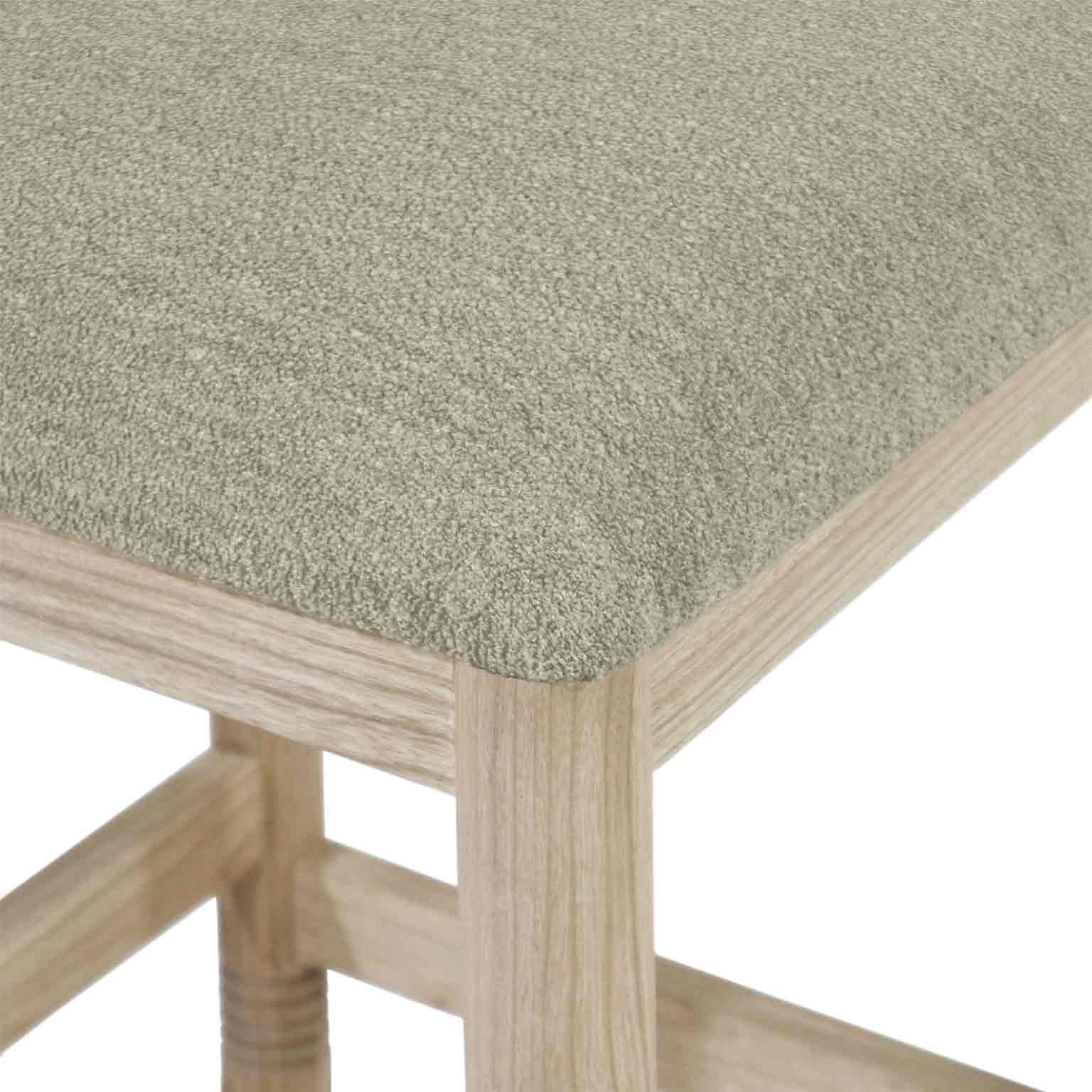 Close-up of beige-taupe bouclé upholstery on a rounded seat edge with natural oak leg and stretcher, showing boucle texture and light oak wood grain.