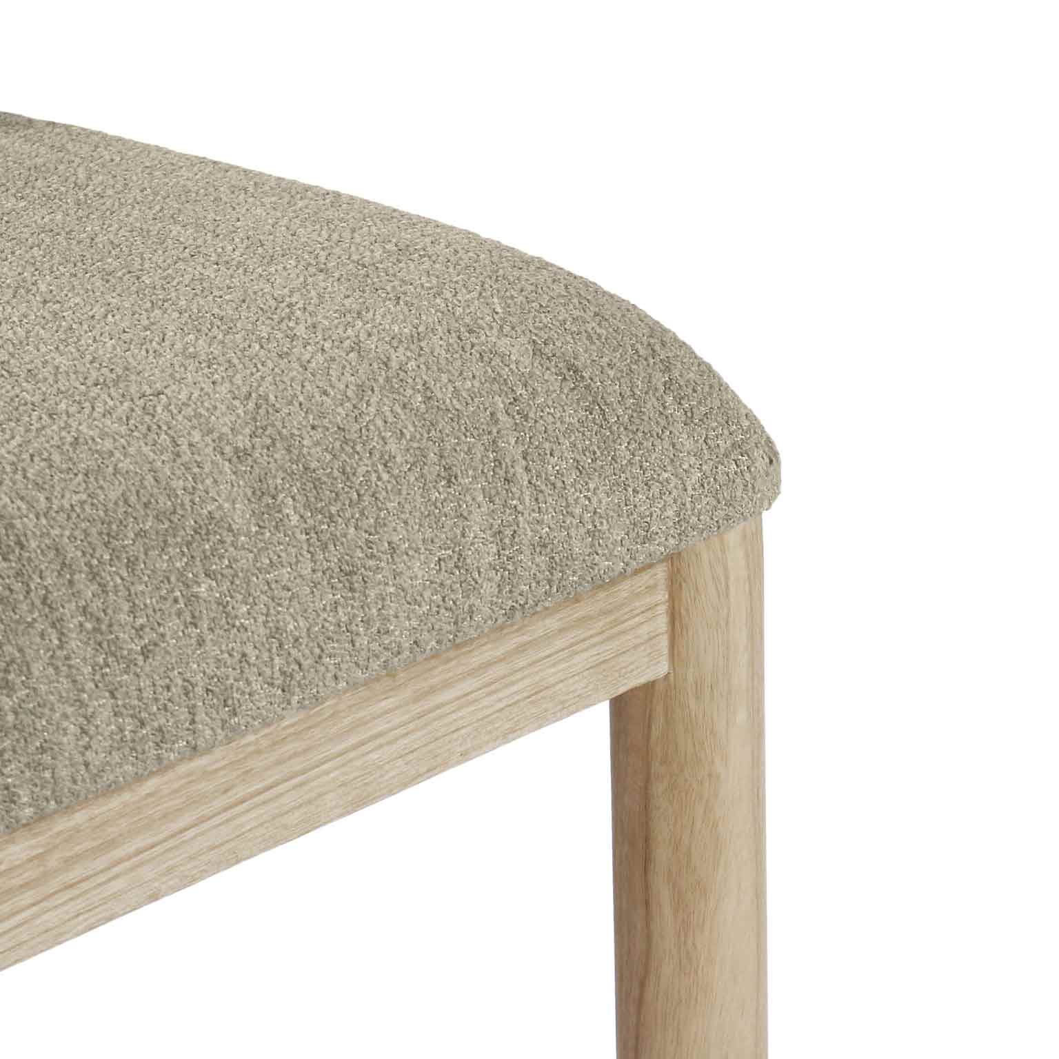 Close-up of a beige bouclé upholstered seat corner on a natural oak frame, showing the textured bouclé fabric and rounded oak leg with visible wood grain.