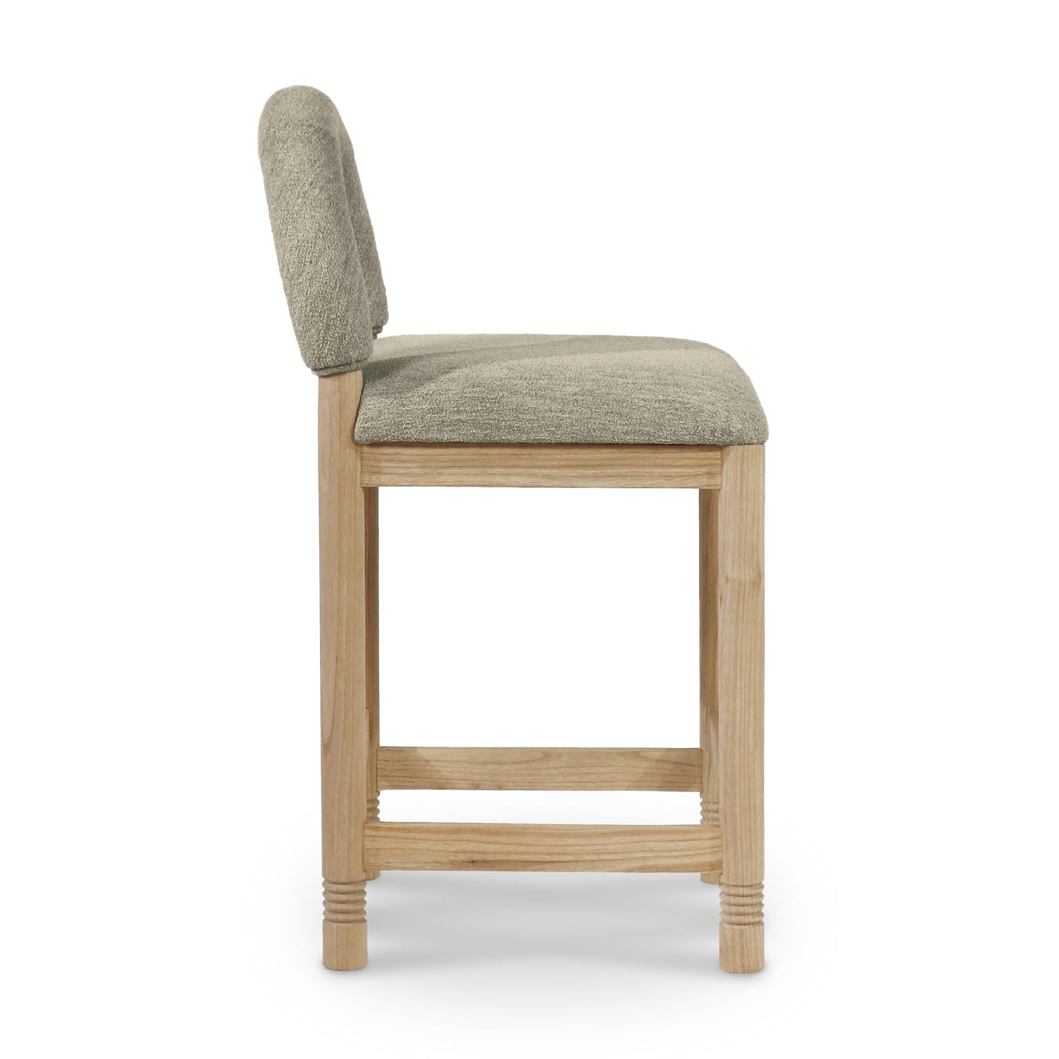 Side view of a counter stool upholstered in taupe boucle with a low rounded back, cushioned seat and natural oak frame featuring stretcher footrests and subtle carved leg detailing.