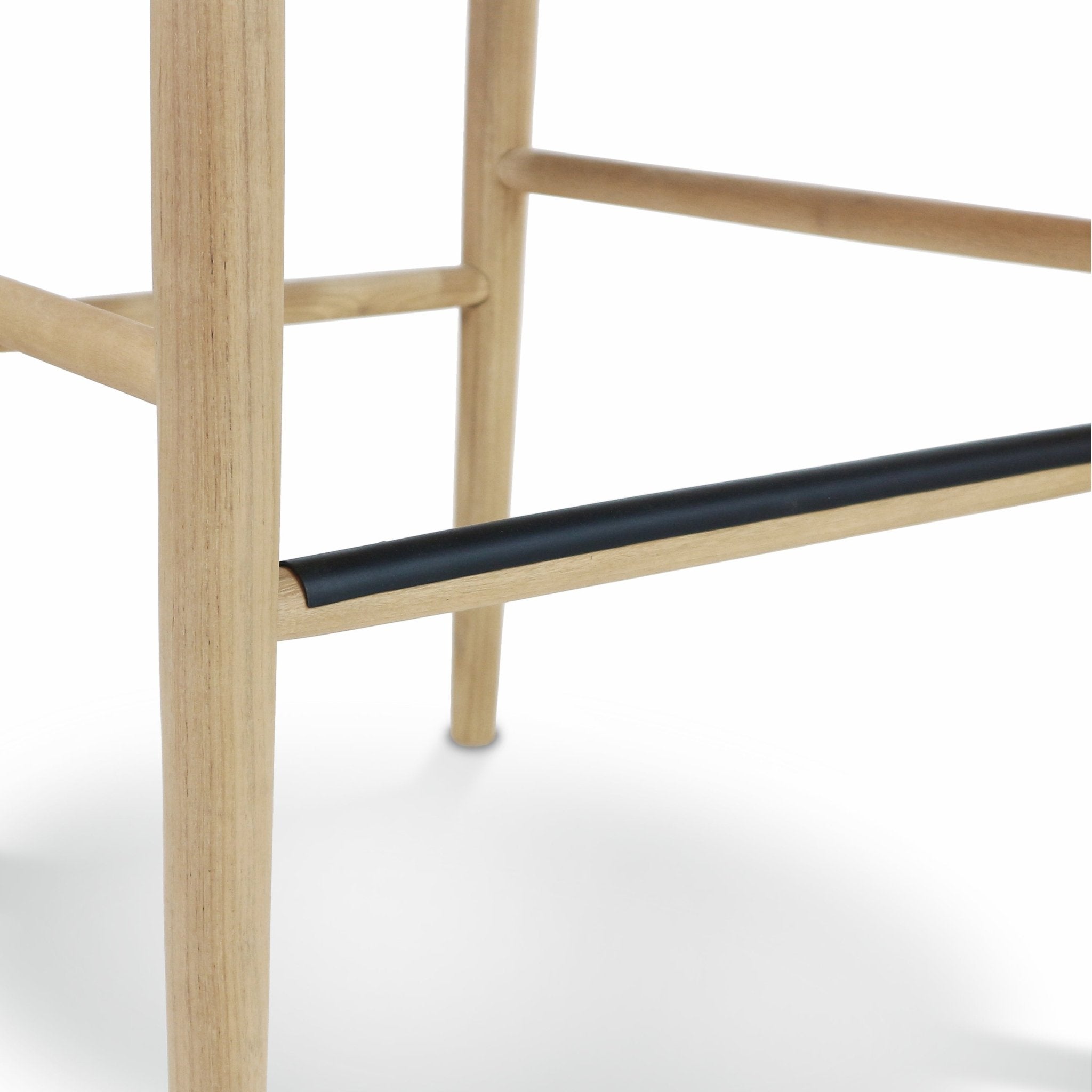 Close-up of a natural wood stool leg and horizontal stretchers featuring a black metal footrest sleeve.