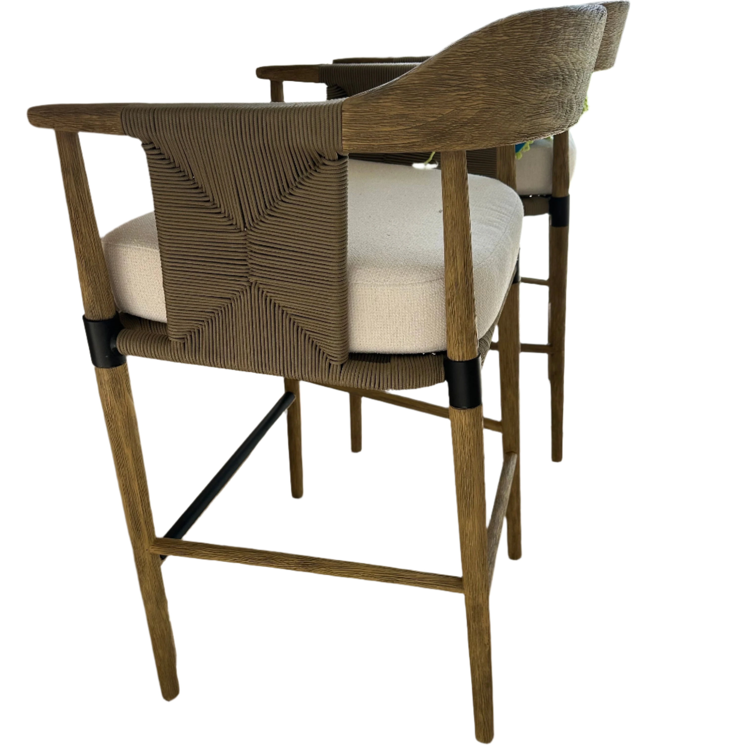 Side view of a natural wood counter stool with a woven rope back panel, curved wooden arms, beige upholstered seat cushion and a black metal footrest, showing tapered legs and woven detailing.