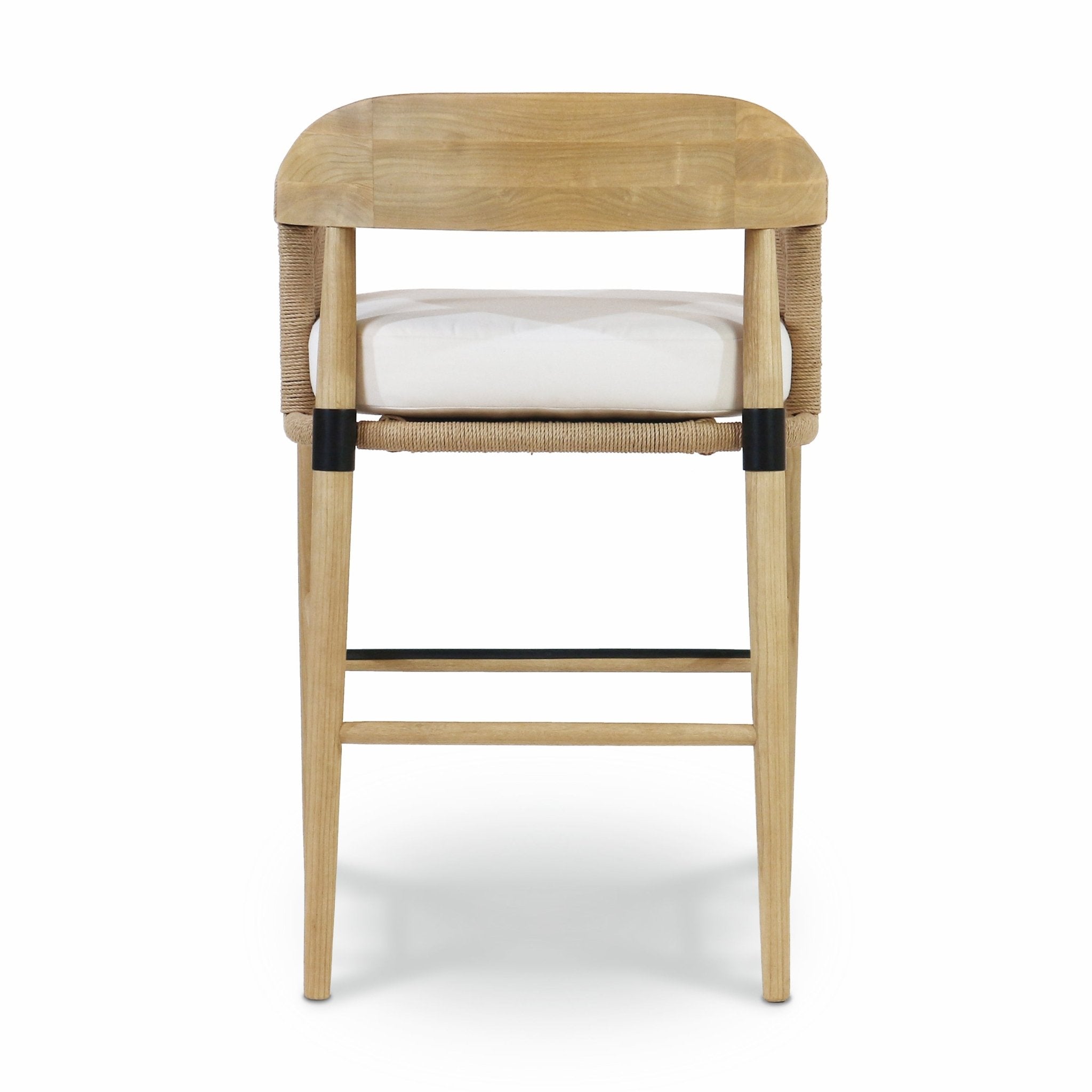 Rear view of a natural teak-framed bar stool with woven rope back, white fabric seat cushion, tapered natural wood legs, and black metal footrest and leg collars.