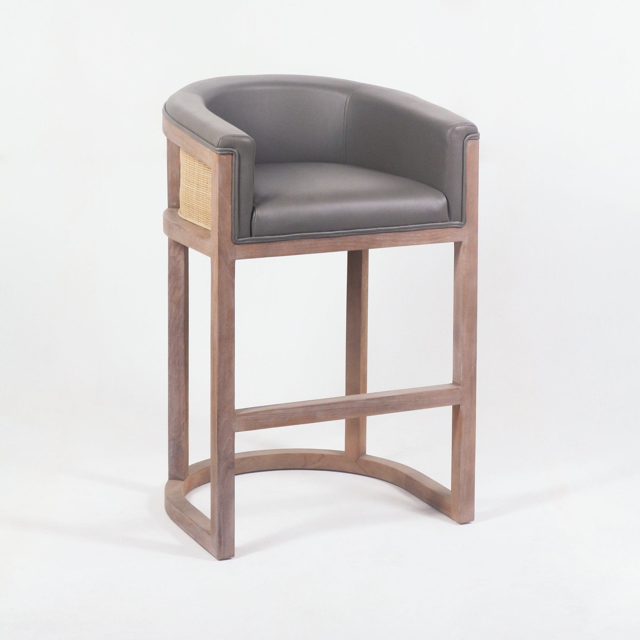Mid-century teak bar stool with curved charcoal faux-leather seat and back, woven cane side panels and natural wood frame with a rounded footrest base.