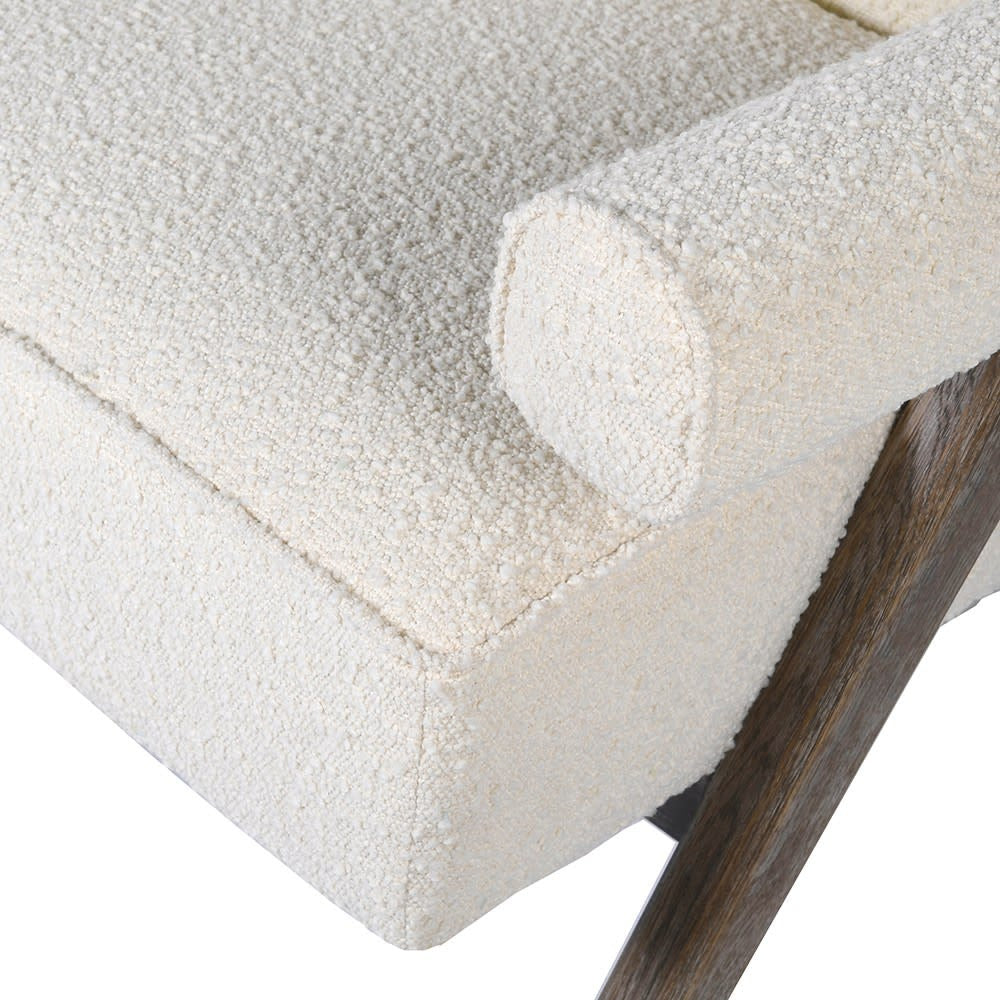 Close-up of a cream boucle-upholstered accent chair seat with a cylindrical bolster cushion showing textured looped fabric, paired with a stained natural wood leg visible at the corner.