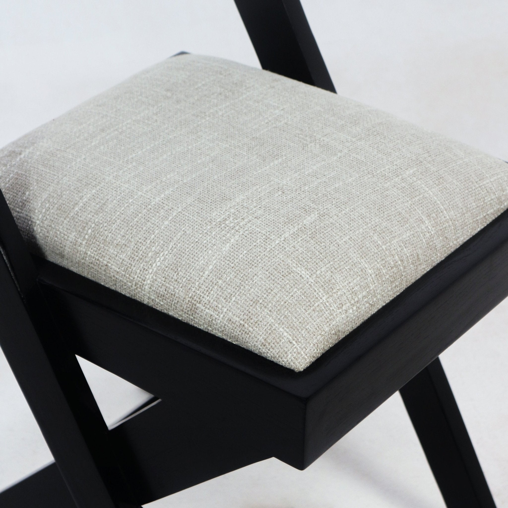 Close-up of a beige textured upholstered seat cushion on a black wooden side chair frame, showing the fabric weave and seat edge detail.