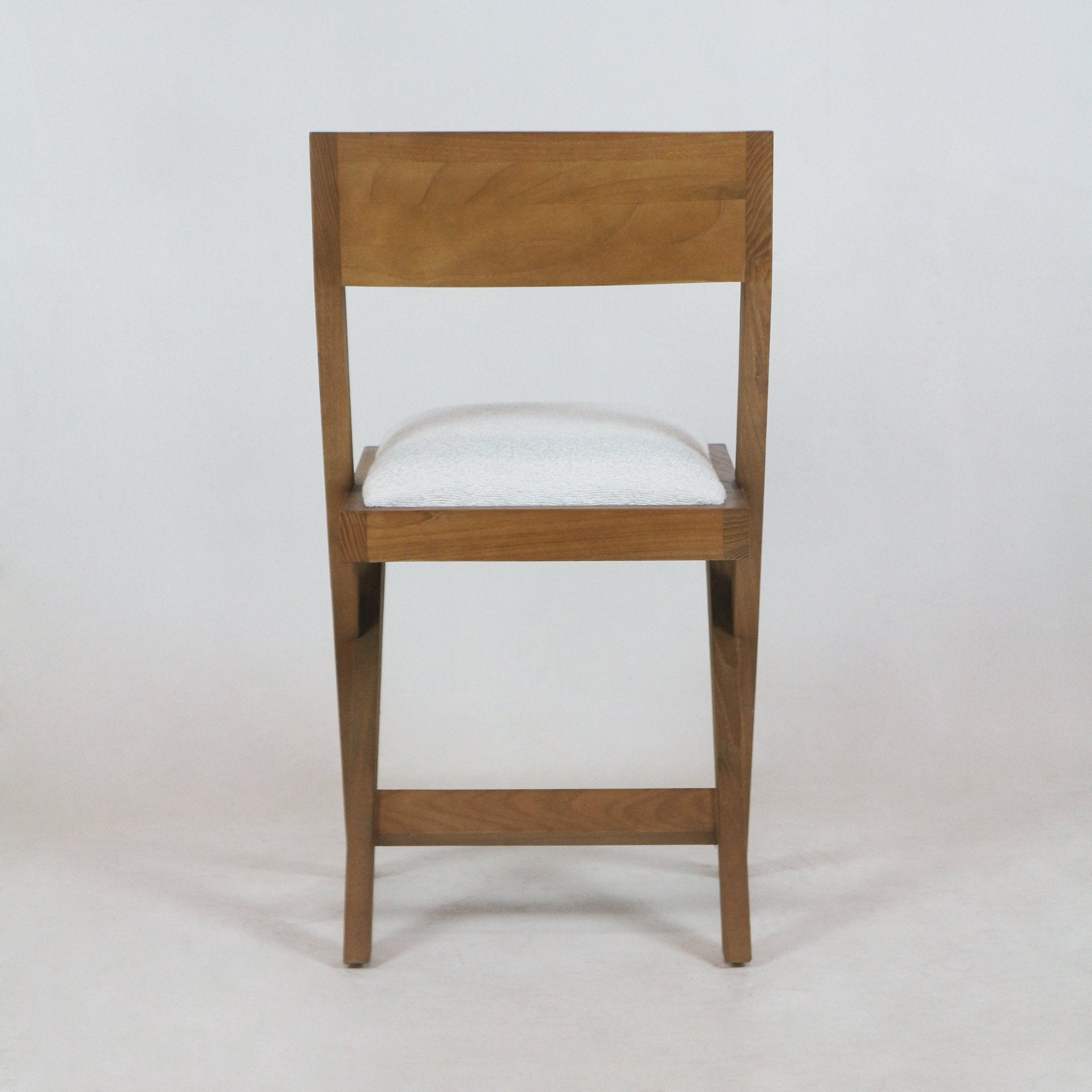 Front view of a side chair with a warm teak wood frame and white boucle upholstered seat, straight wooden backrest and tapered legs in a mid-century modern silhouette.