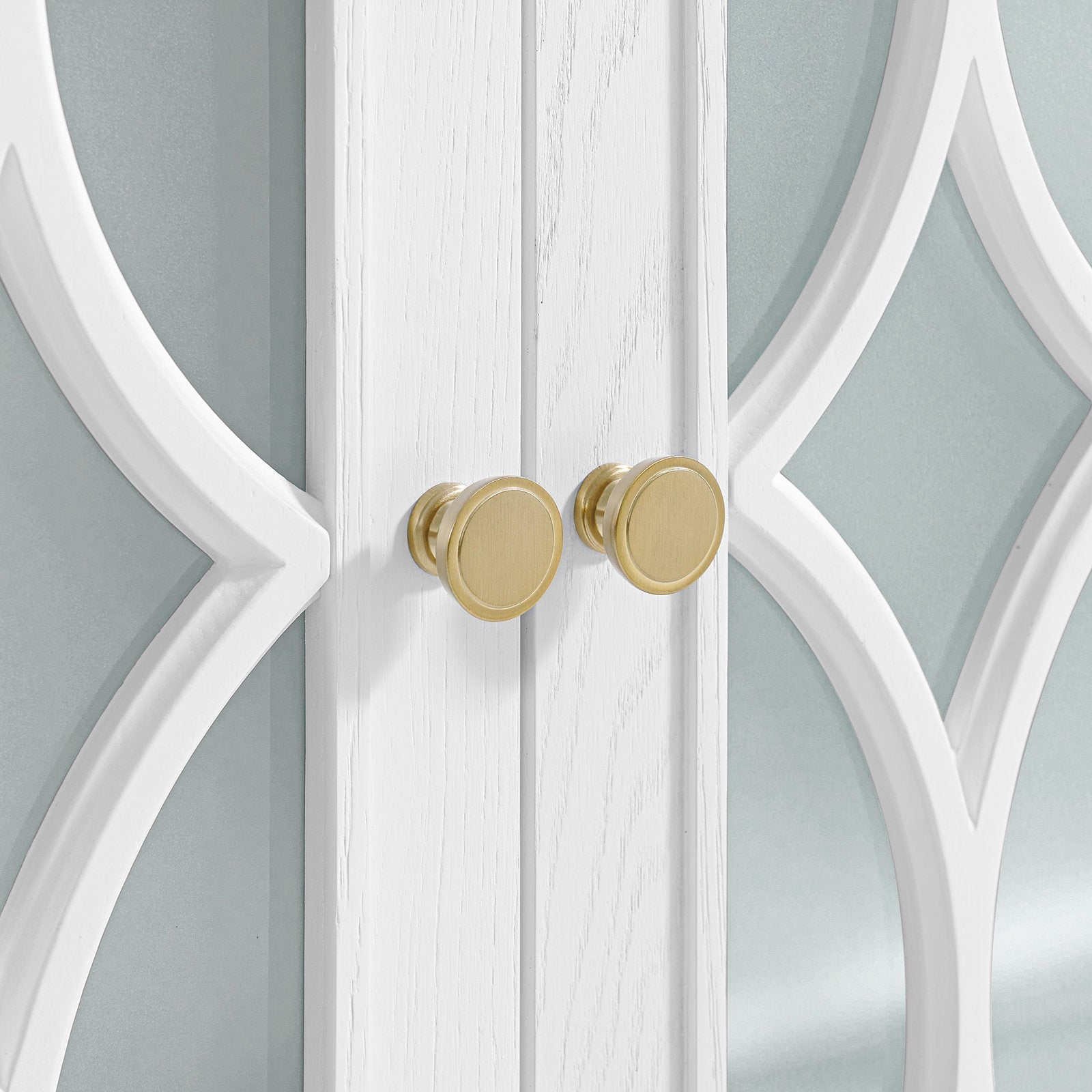 Close-up of modern white solid-wood vanity doors with decorative arched mirror panels and two round brushed brass knobs.