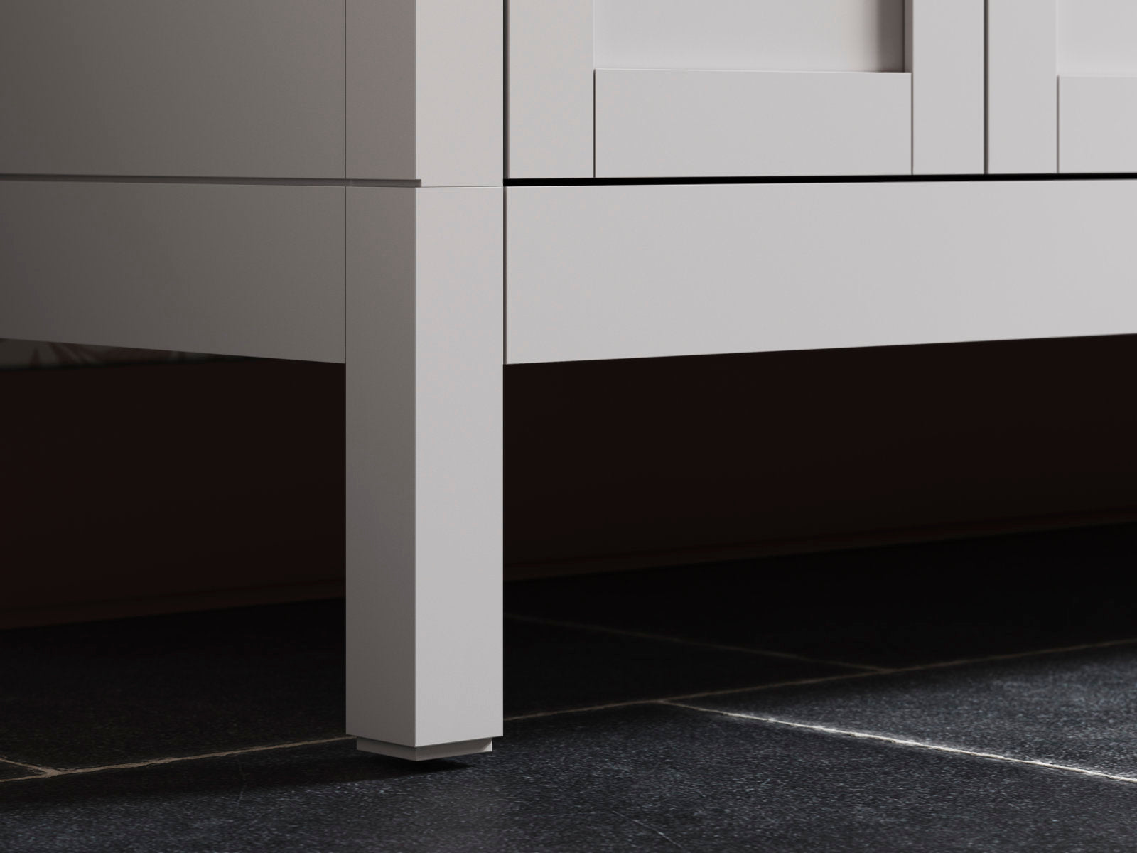 Close-up of the lower corner and square leg of a stone-colored solid wood modern bathroom vanity, showing the recessed base and small plinth resting on a dark tiled floor.