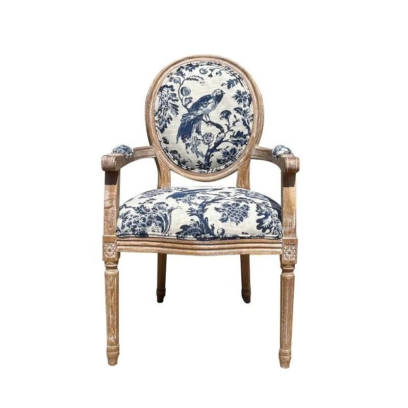 Front view of a French-style teak dining armchair with a weathered natural wood frame and blue-and-white toile linen seat and round back featuring a bird and floral motif.