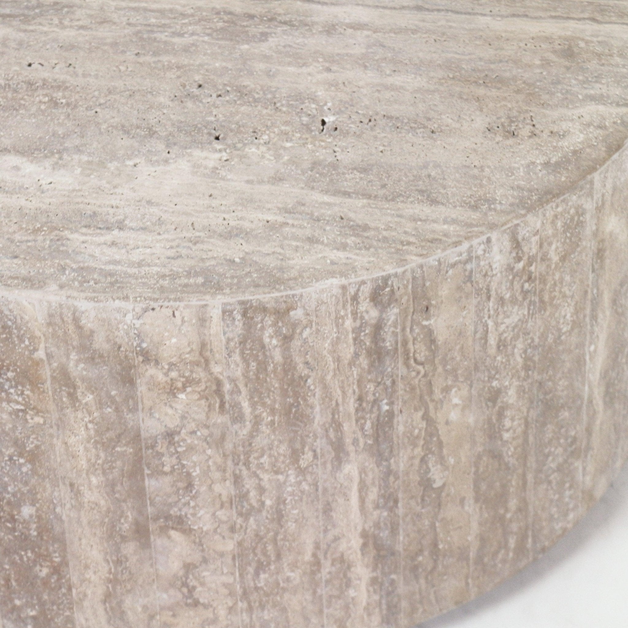 Close-up of a round travertine coffee table top and edge showing natural beige stone veining and textured surface.
