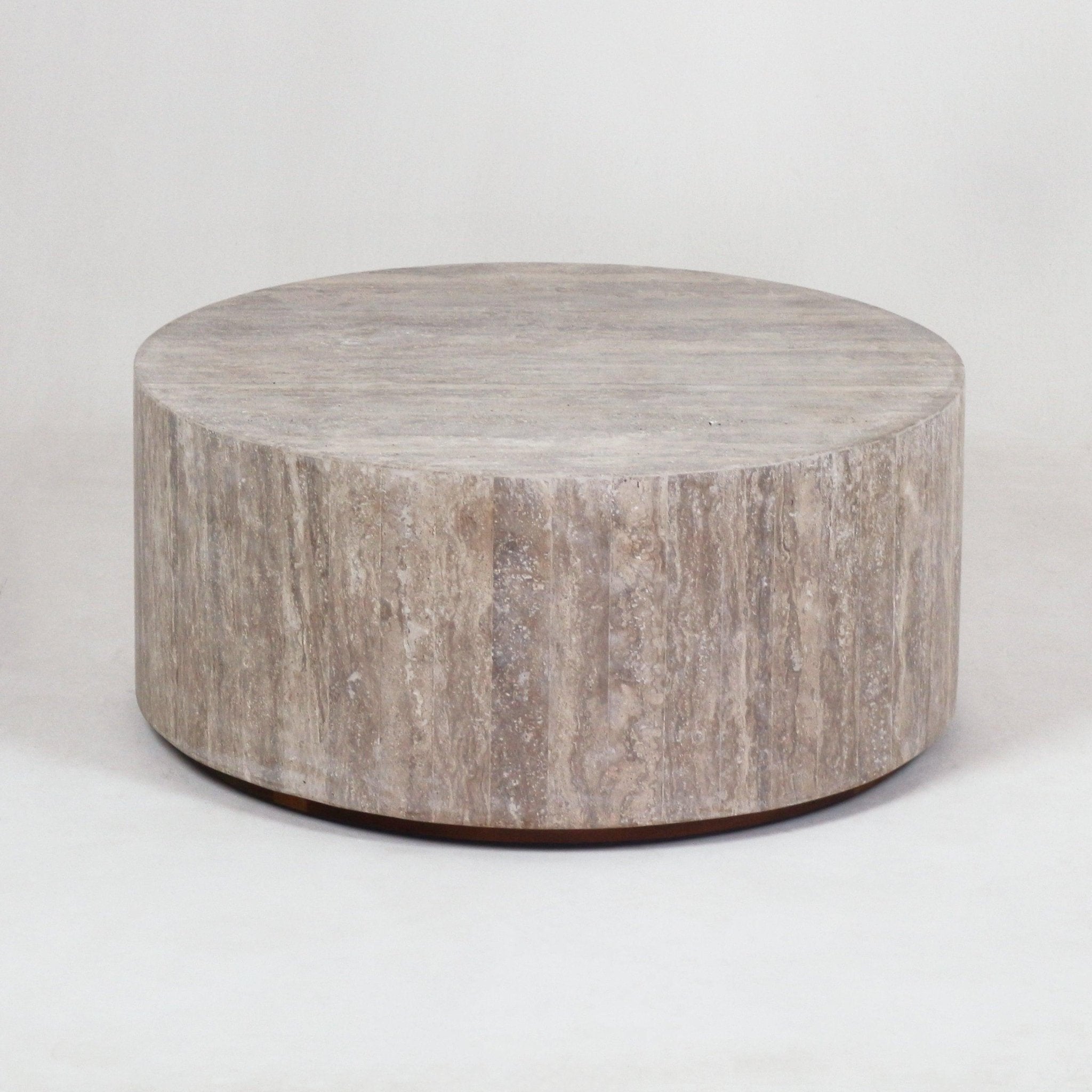 Low round travertine coffee table in natural beige stone with a full-height cylindrical base and smooth flat top, shown in a minimalist modern style against a neutral background.