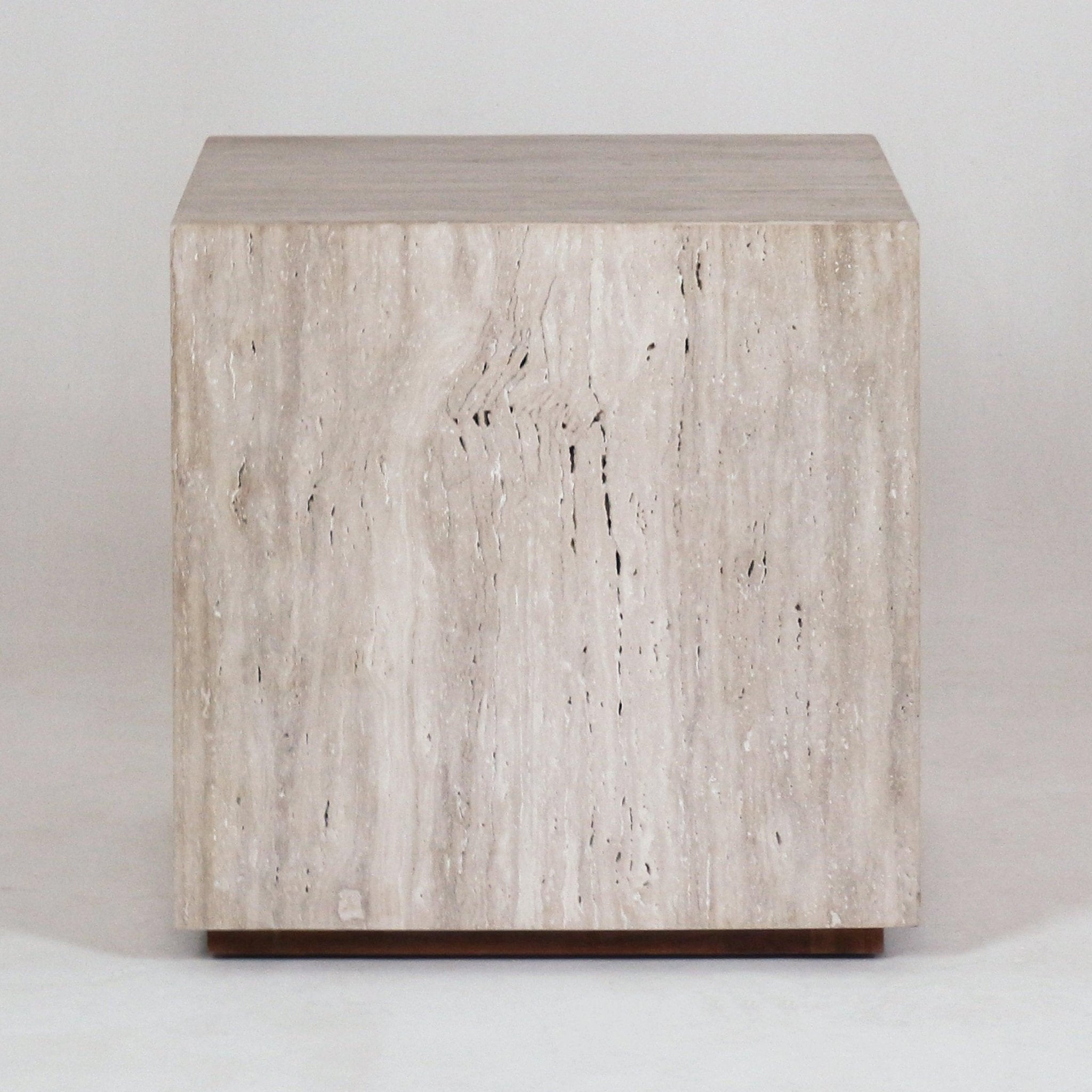 Front view of a cube-shaped travertine nightstand in natural beige stone with vertical veining, resting on a slim wood base for a minimal modern bedside table.