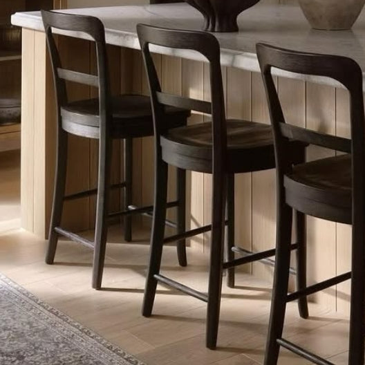 Three mahogany solid-wood counter-height bar stools with full curved backs and round seats arranged along a light-wood kitchen island topped with a marble countertop.
