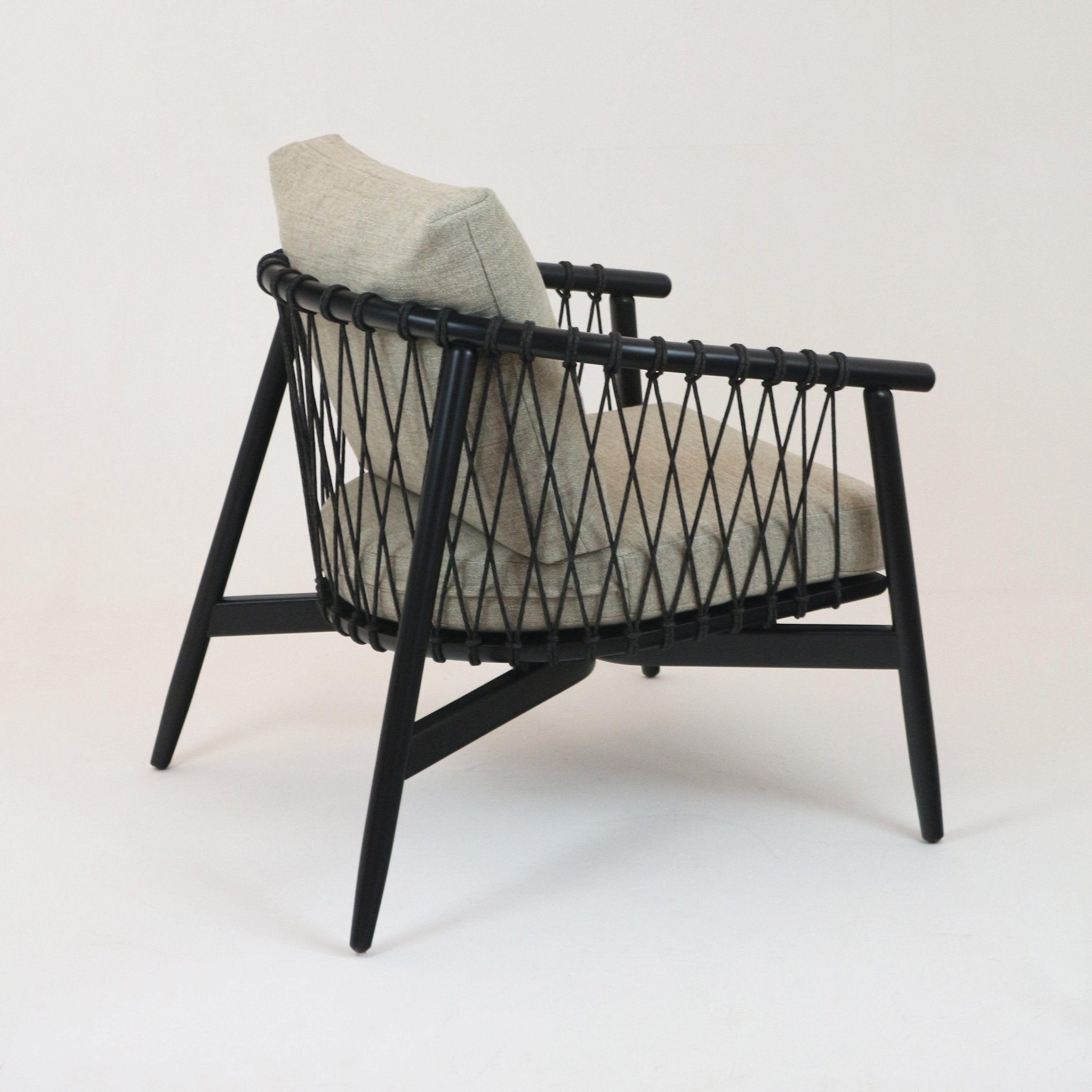 Modern lounge chair with beige alpaca boucle upholstery, black solid wood frame and crisscross black rope sides, angled legs and slim armrests in a contemporary accent chair silhouette.