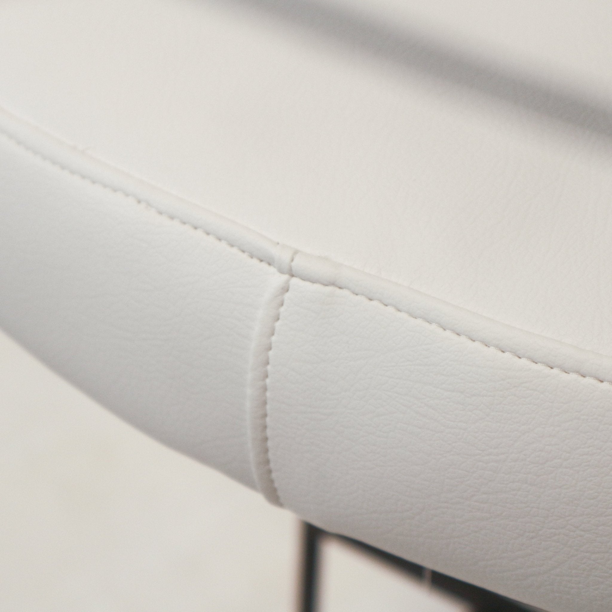 Close-up of a white faux leather counter stool seat showing stitched seam detail, subtle grain texture and a portion of the slim black metal leg.