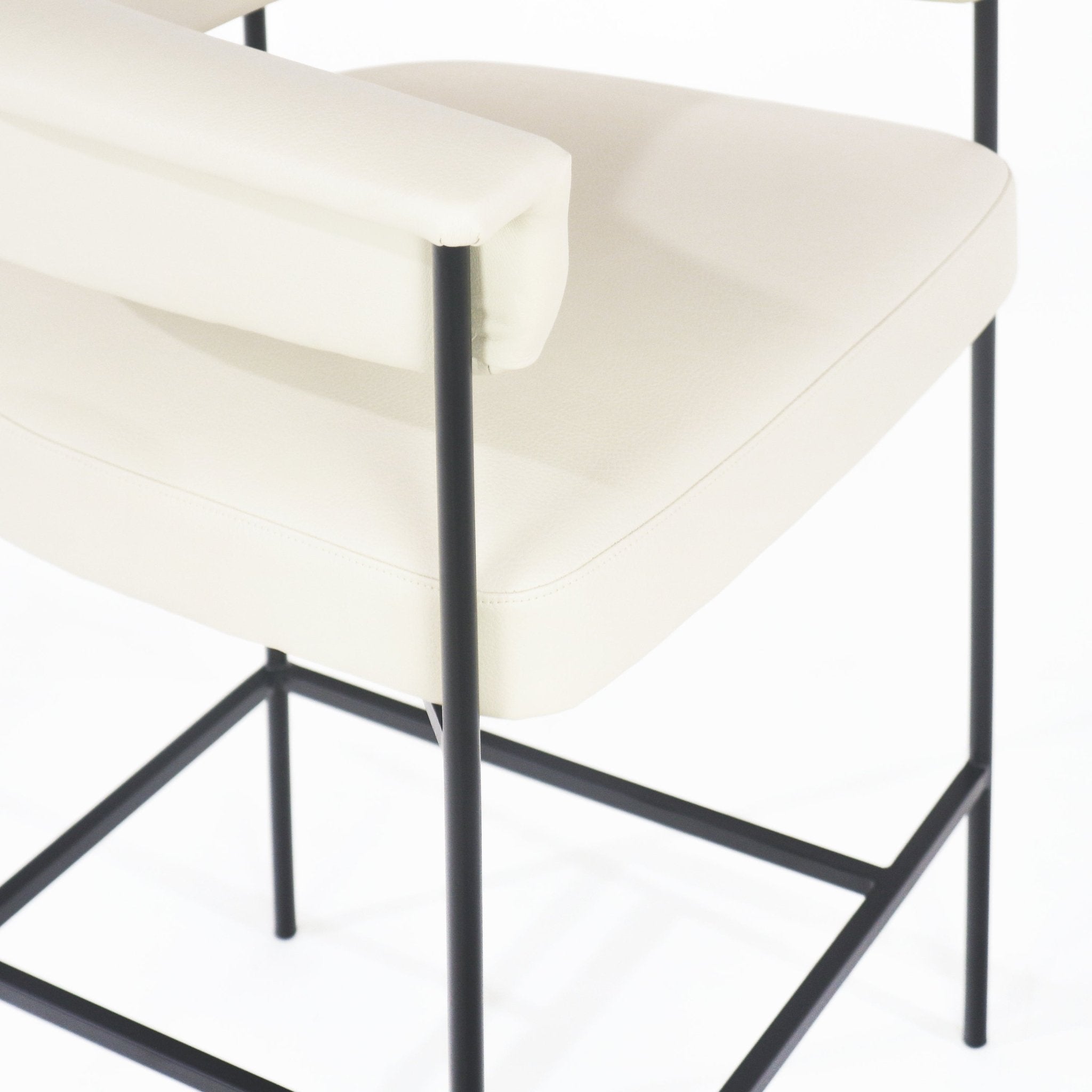 Close-up of a cream faux-leather counter stool showing the padded seat and backrest on a slim black metal frame with square footrest.