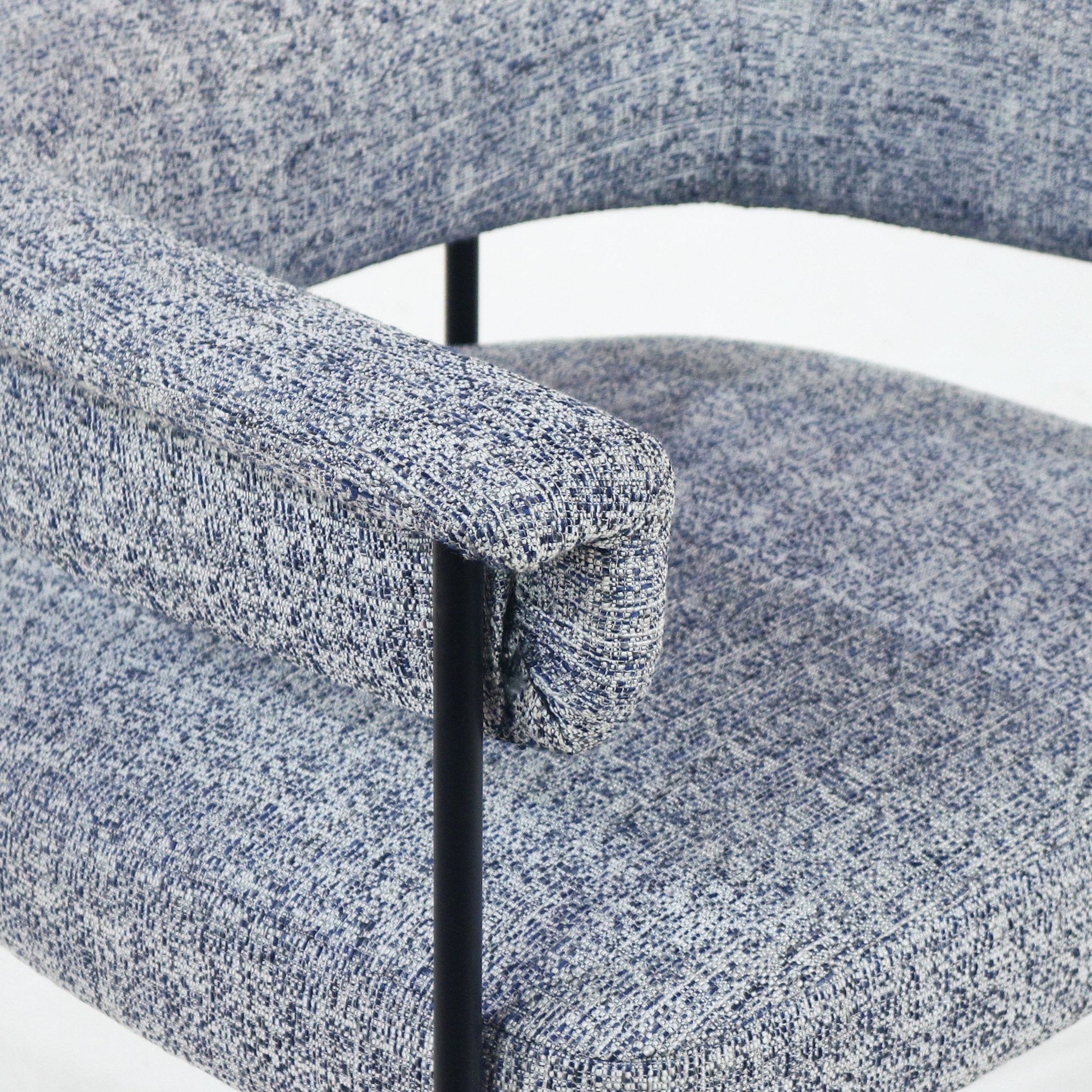 Close-up of a gray boucle upholstered dining chair showing the padded seat and curved armrest with a slim black metal support rod, highlighting the textured fabric.