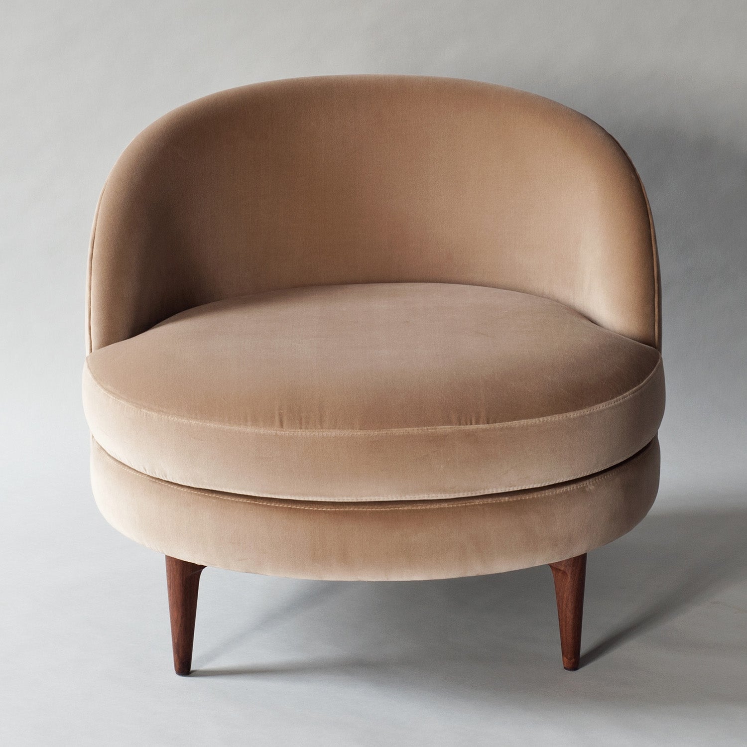 Front view of a blush velvet barrel accent chair with a full curved back, round cushioned seat, and tapered solid wood legs.