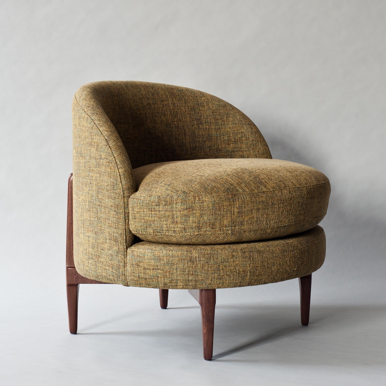 Modern curved barrel accent chair upholstered in textured green-gold tweed fabric with a plush round seat cushion and tapered solid wood legs.