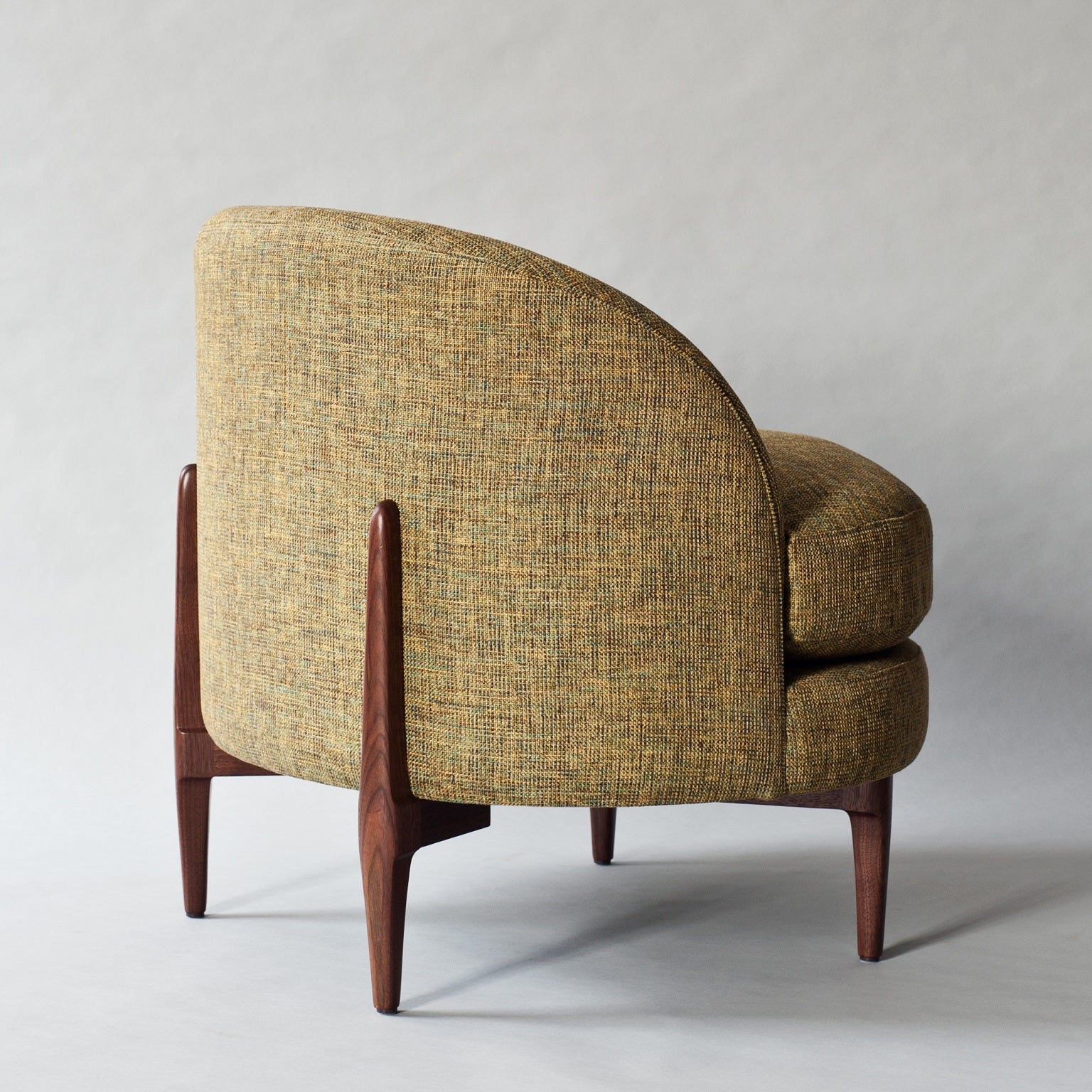 Rear three-quarter view of a modern accent chair upholstered in green boucle fabric with a curved full back, rounded stacked seat cushions and tapered solid wood legs in a dark finish.