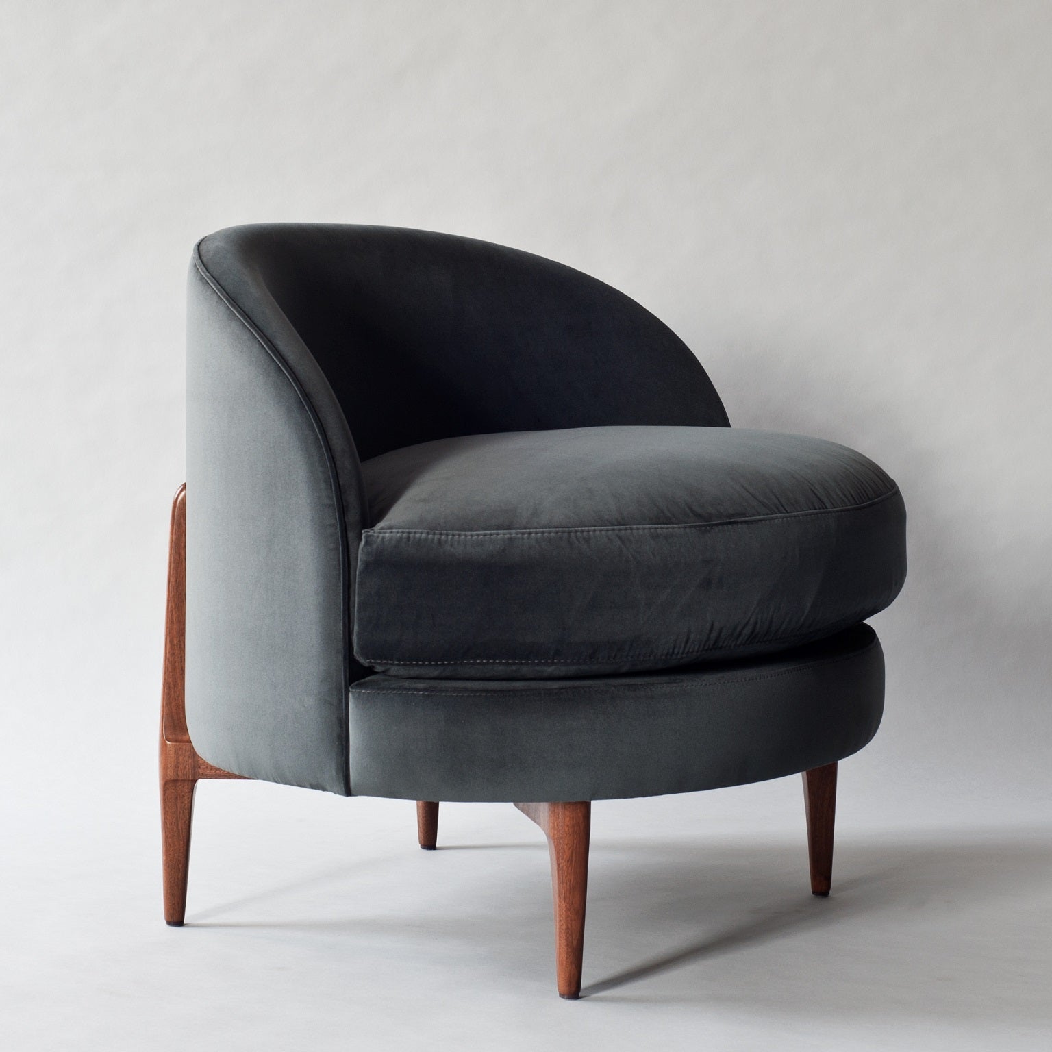 Dark gray velvet accent chair with a curved barrel back, plush rounded seat cushion and exposed solid wood tapered legs.