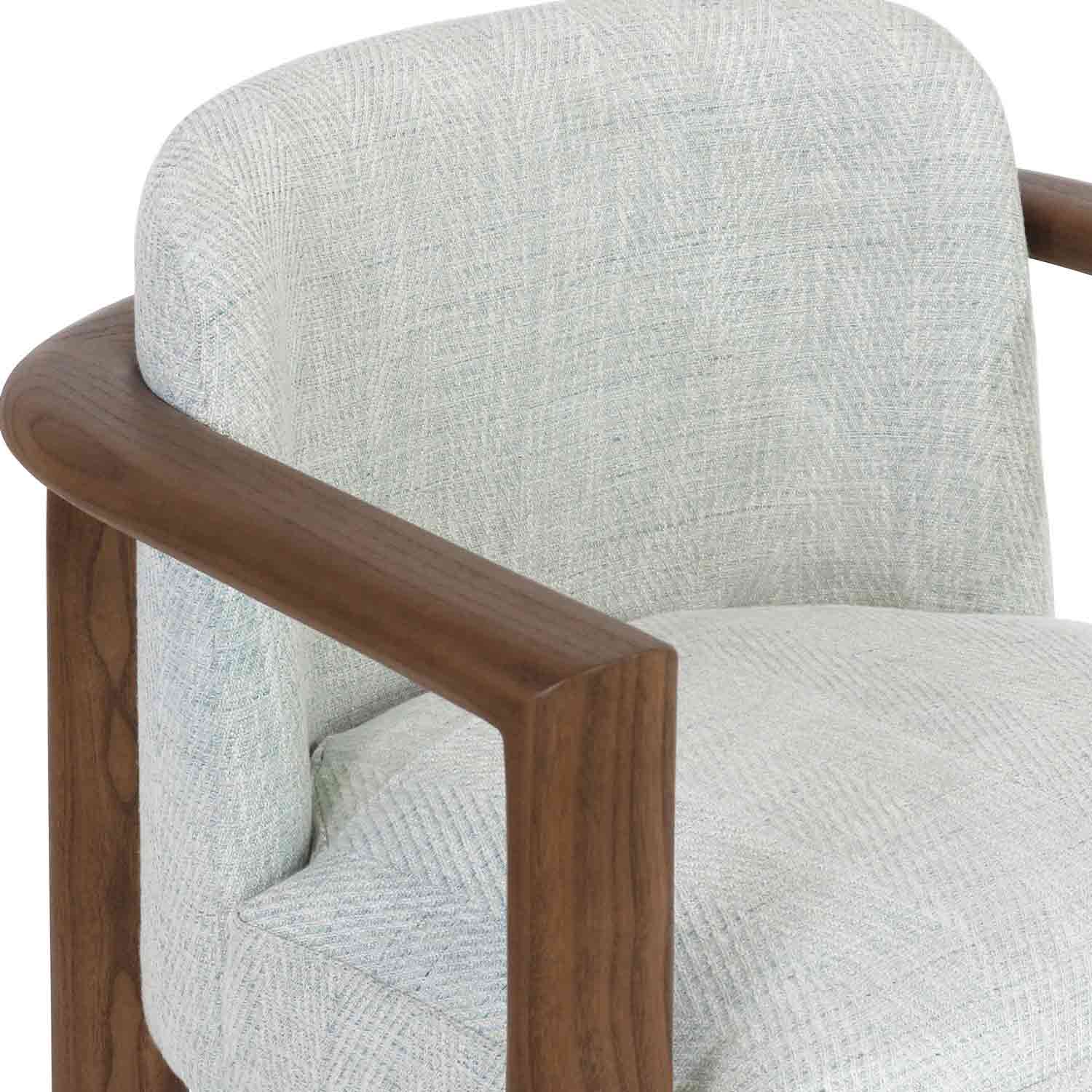 Close-up of a modern dining chair showing a rounded oak arm and light neutral herringbone fabric upholstery over a cushioned full back and seat.