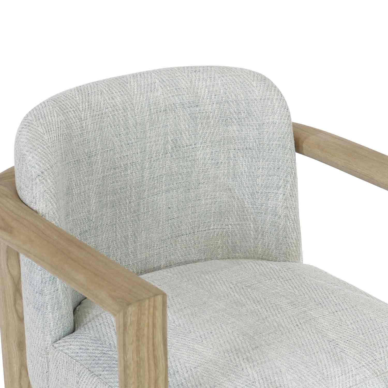 Close-up of a modern upholstered dining chair showing light herringbone-patterned fabric on the seat and curved back with natural oak wooden arms and frame.