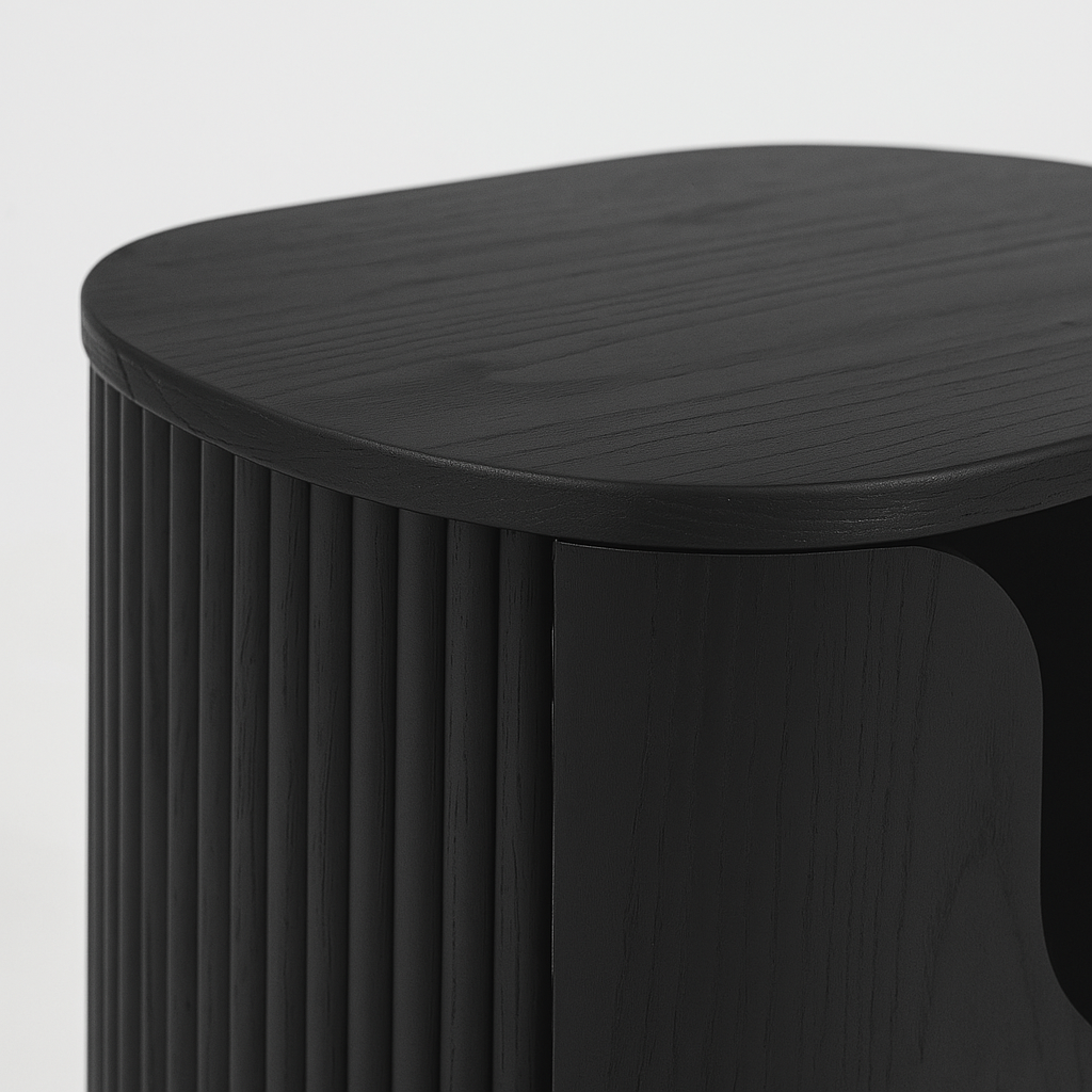 Close-up of a black solid wood nightstand top and fluted front, showing rounded edges, visible wood grain, and a curved door detail in a modern Scandinavian style.