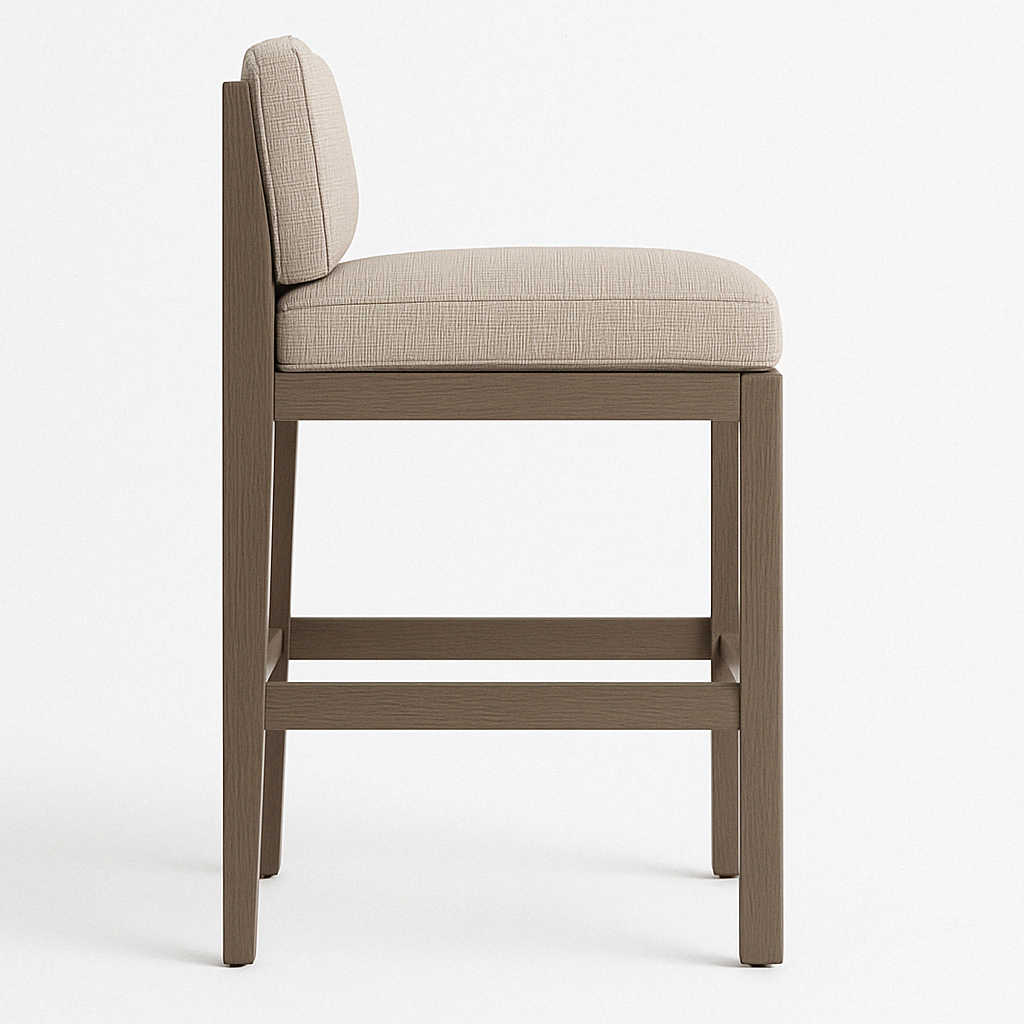 Side profile of an armless teak outdoor bar stool with linen-like beige upholstery, low cushioned back, tapered teak legs and double horizontal footrest in a natural teak finish.