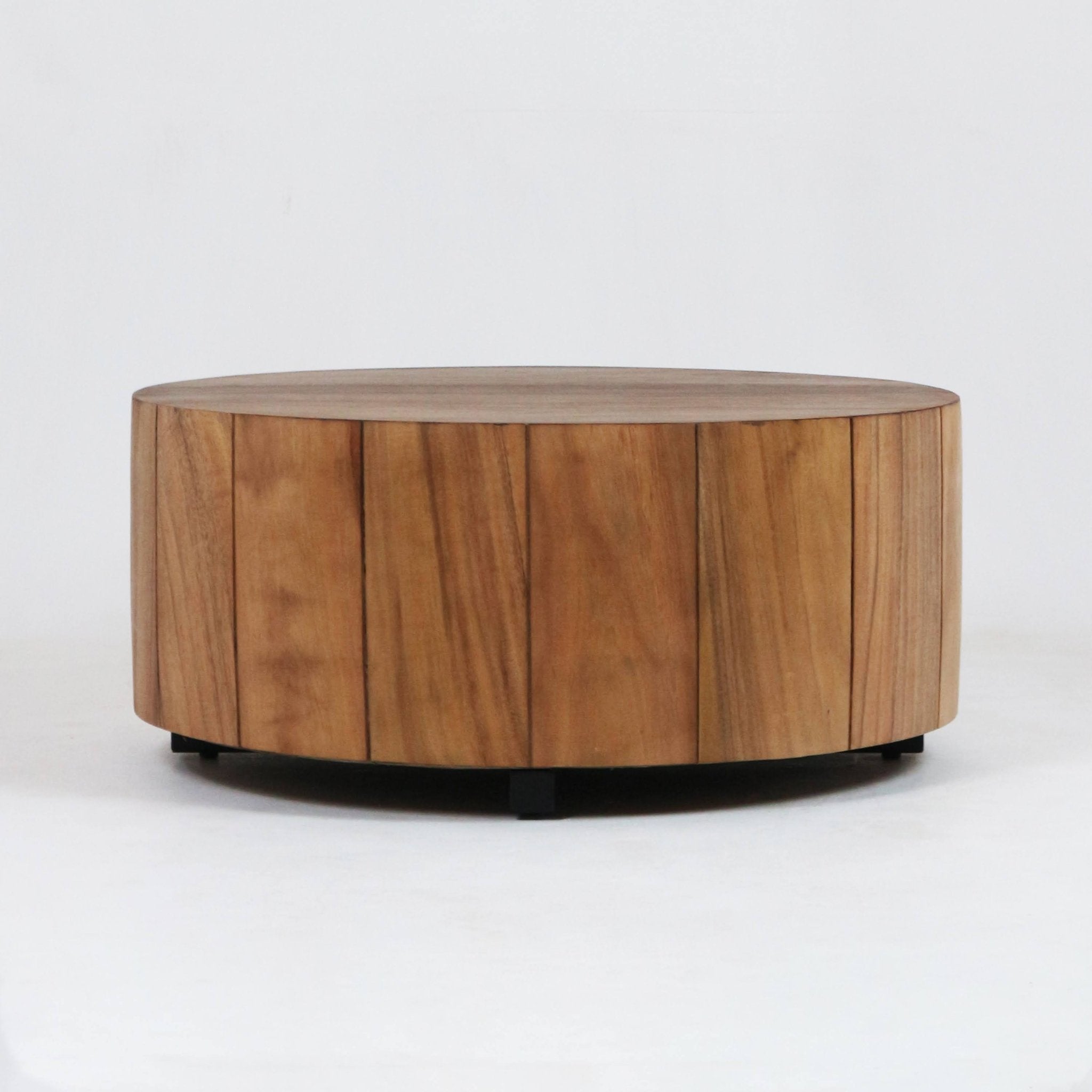 Low, round solid wood coffee table with vertical plank panels and a natural brown finish, supported by a low black metal base against a plain white background.