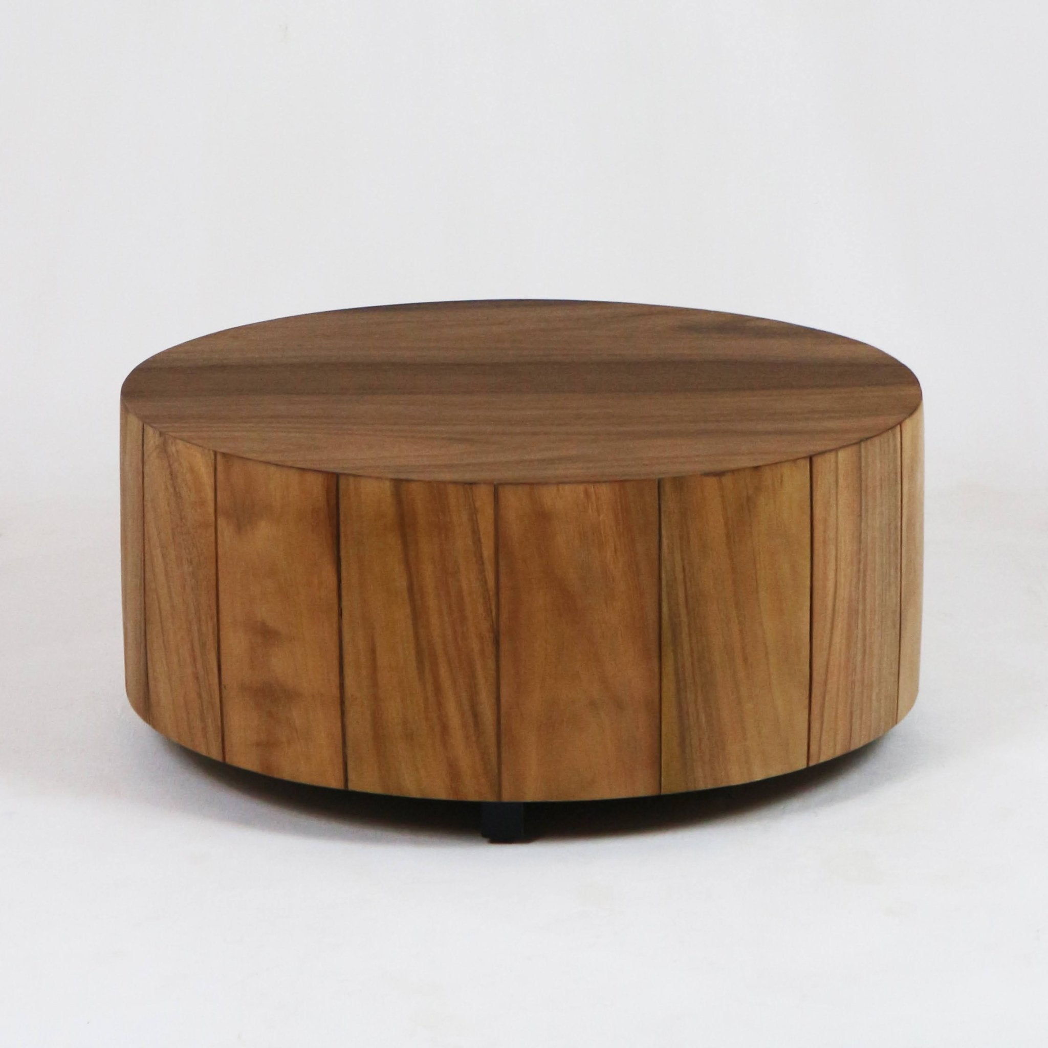 Round solid wood coffee table with vertical plank-style sides, smooth warm natural wood top and low black feet in a modern low-profile design, shown on a plain white background.